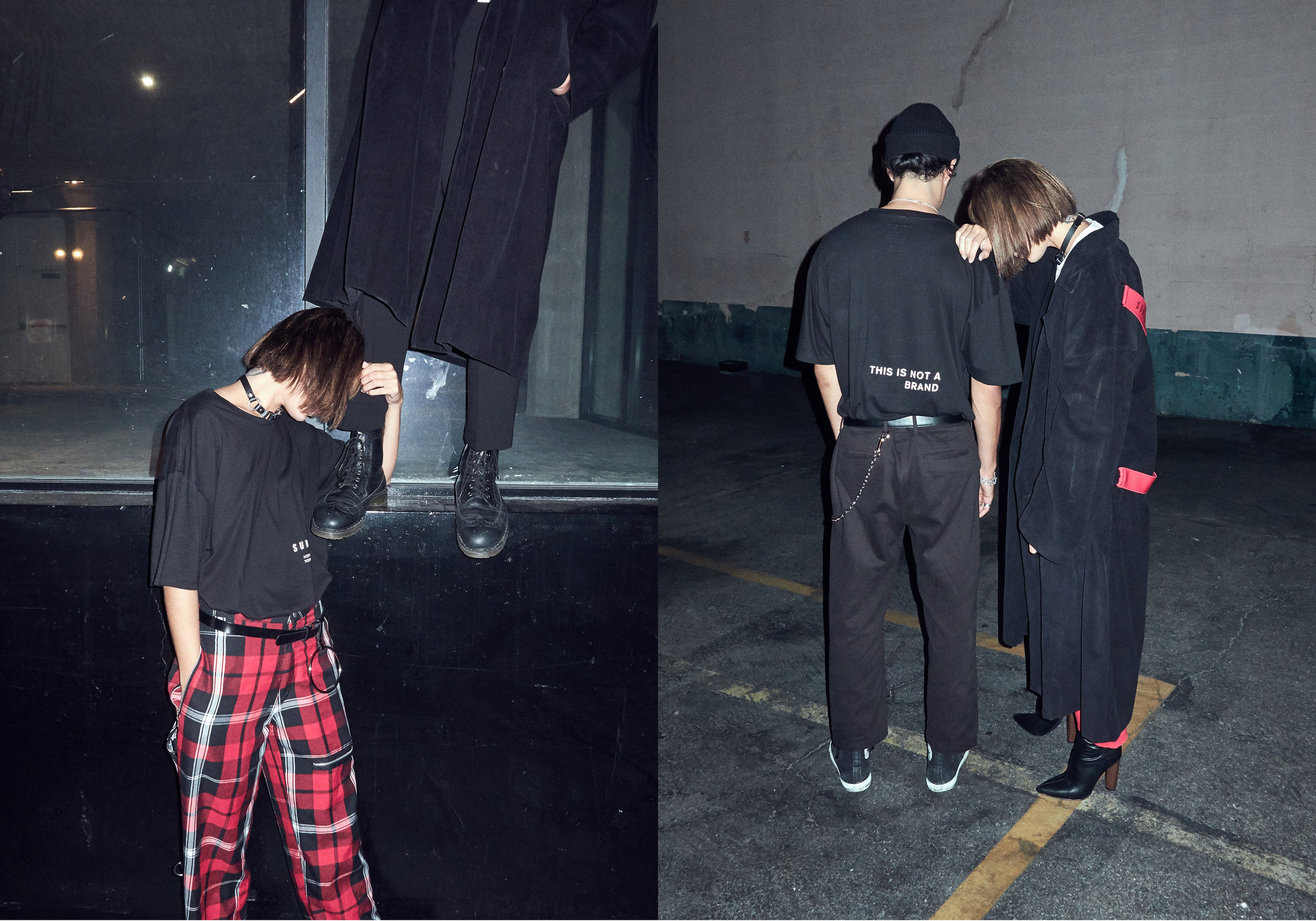 Two individuals dressed in dark streetwear clothing stand together in an urban setting at night. One person wears a black shirt with the text 'THIS IS NOT A BRAND' and a chain belt, while the other is in a black coat with red accents and high-heeled 