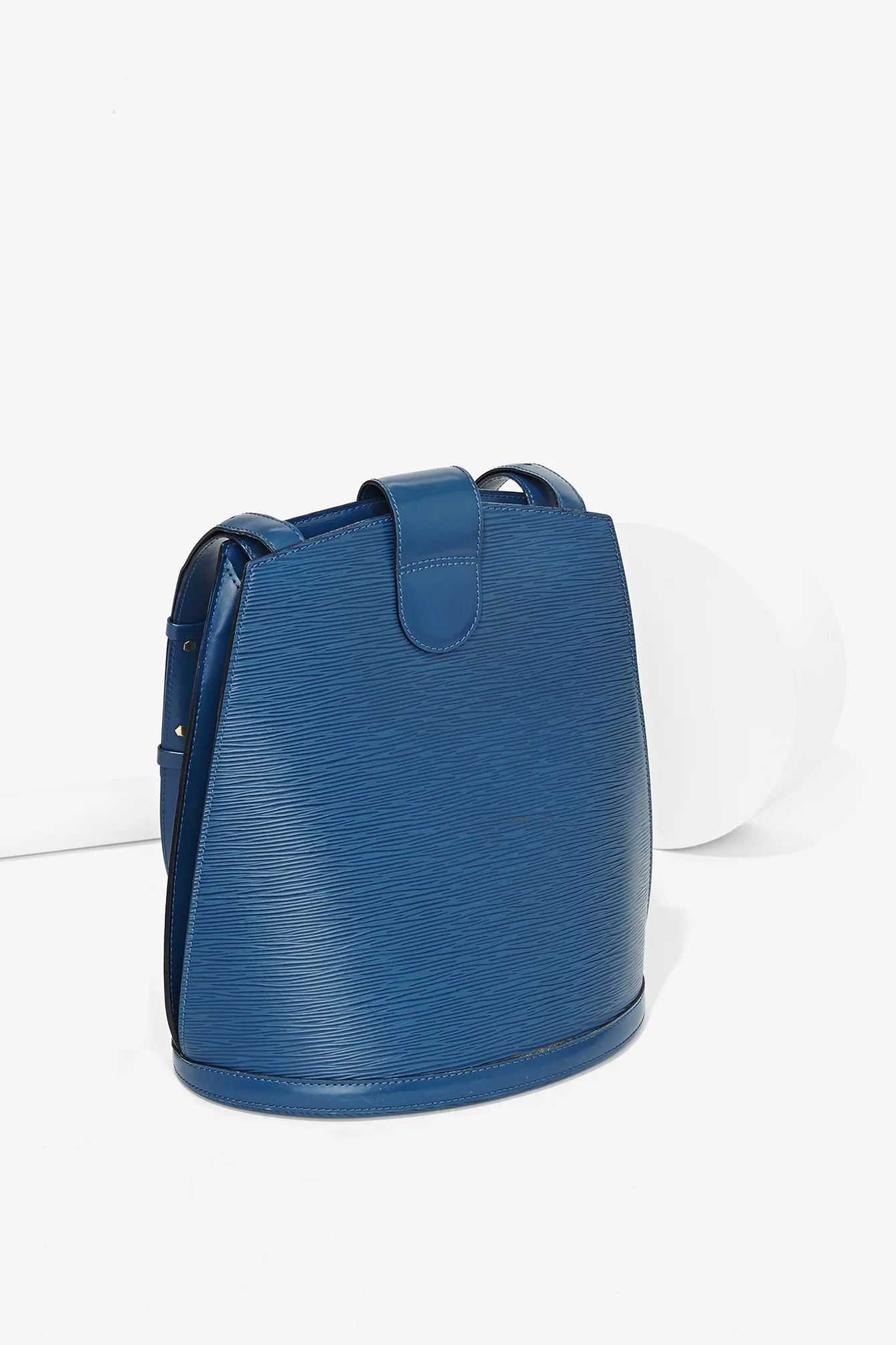 Blue textured leather handbag against white background with two white spherical objects nearby.