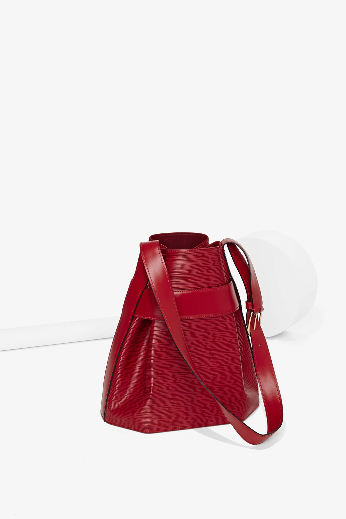 Red designer handbag with textured leather design, set on a white background.