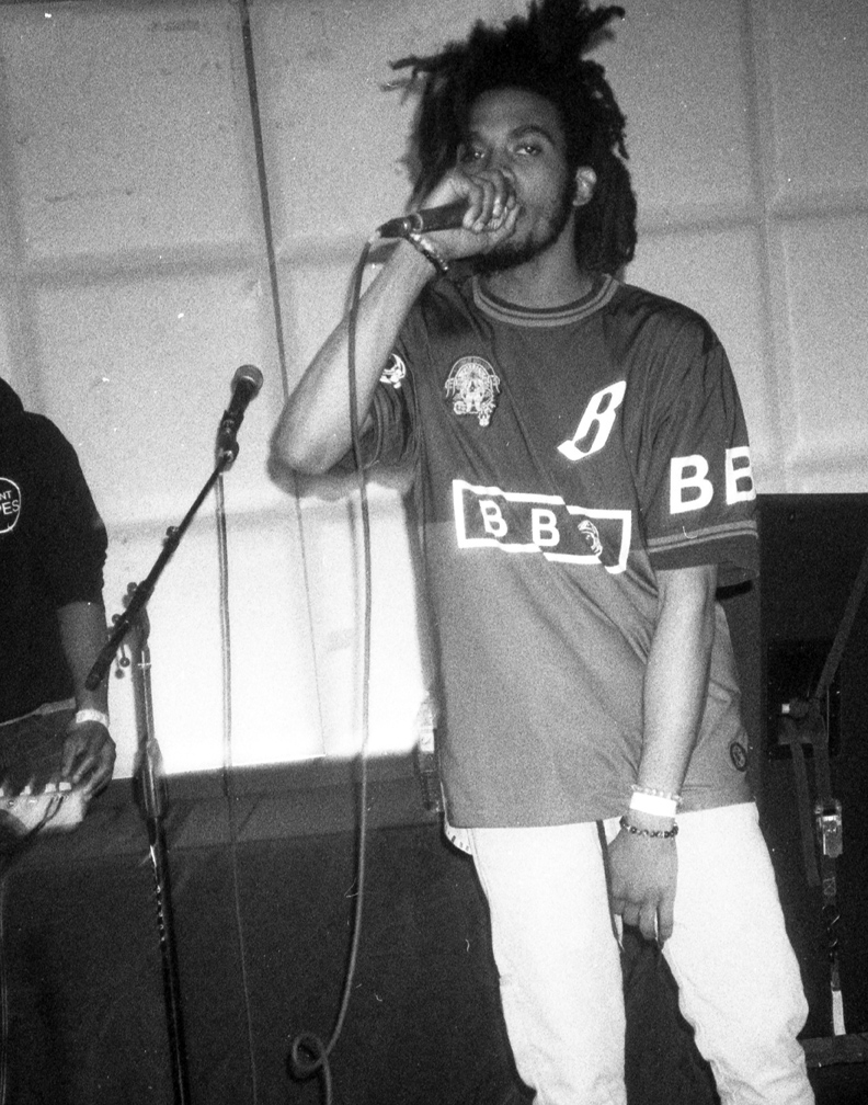 A young man with dreadlocks singing into a microphone during a performance or rehearsal.