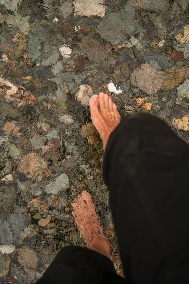 Bare foot stepping into clear shallow stream over stones, representing grounding for nervous system regulation in POTS, ME/CFS, and dysautonomia.