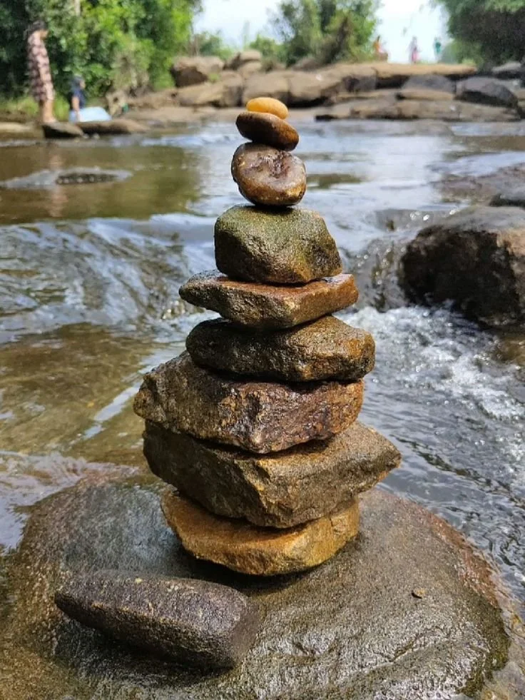 Stack of smooth river stones balanced in a shallow flowing stream, symbolizing nervous system regulation in POTS, MCAS, ME/CFS, autoimmune, and post-viral illness.