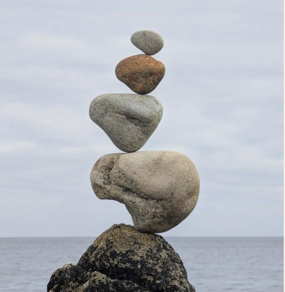 Narrow stack of coastal stones balanced on a seaside rock, representing restored stability and nervous system regulation in ME/CFS, POTS, histamine intolerance, and autoimmune conditions.