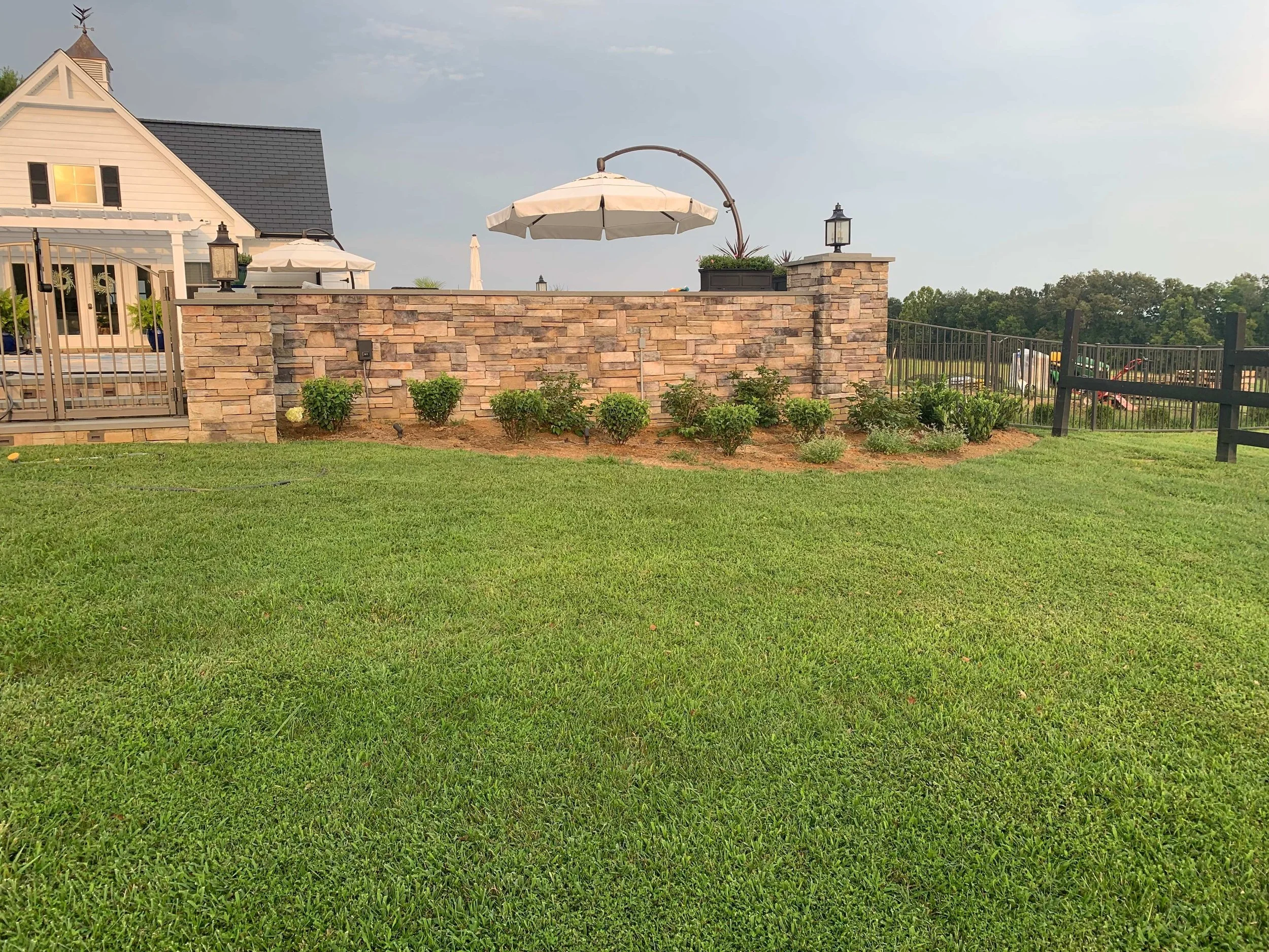 Residential landscape with stone retaining wall, patio area, and manicured lawn in Lynchburg, VA