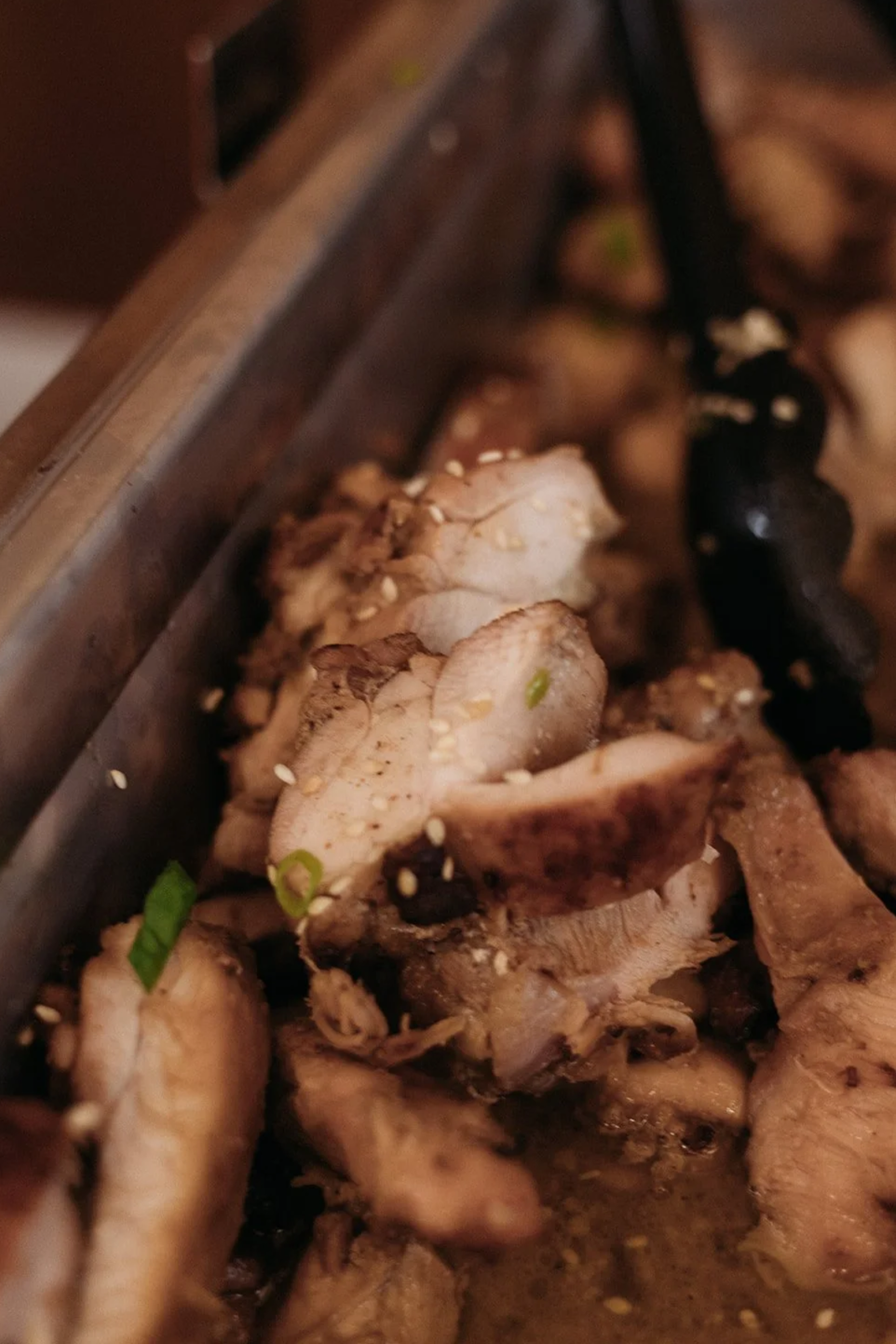 Close-up of cooked sliced chicken with sesame seeds and green onions.