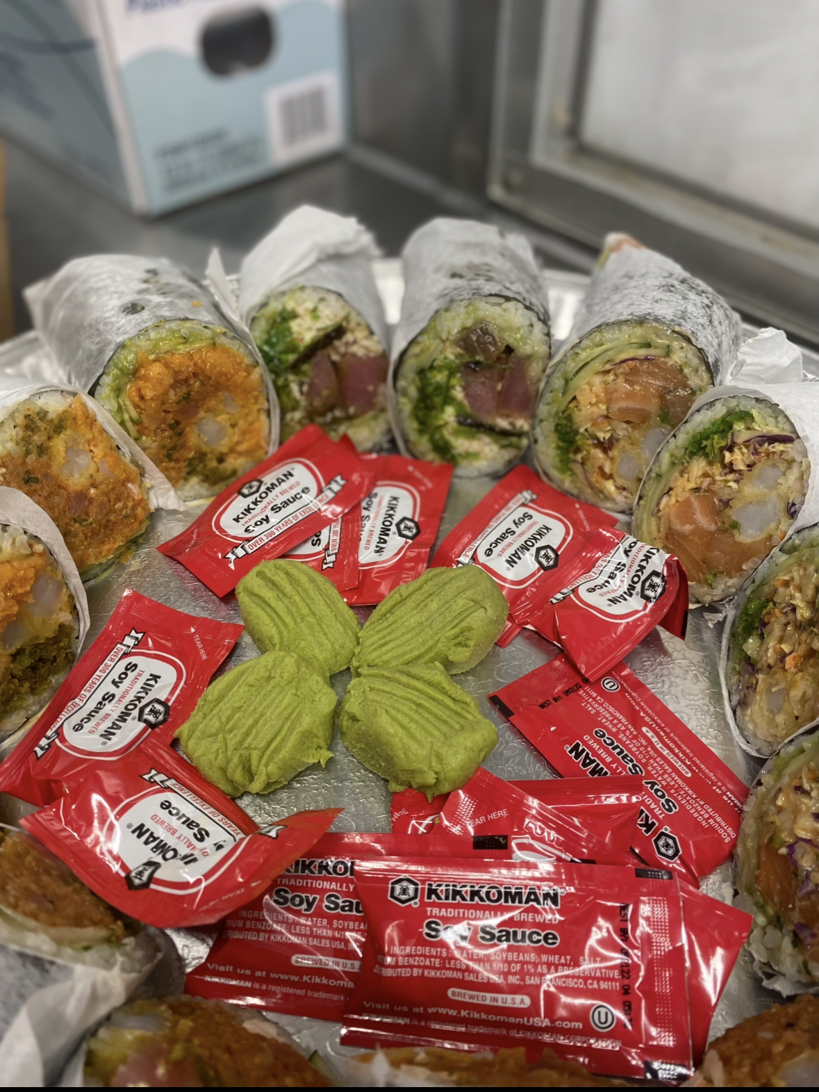 Close-up view of assorted sushi rolls accompanied by red soy sauce packets and green wasabi, arranged on a tray.