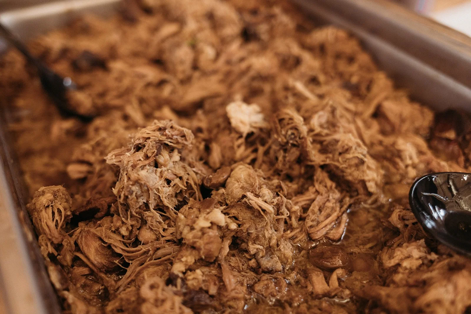 Shredded cooked meat in a tray with a black serving spoon