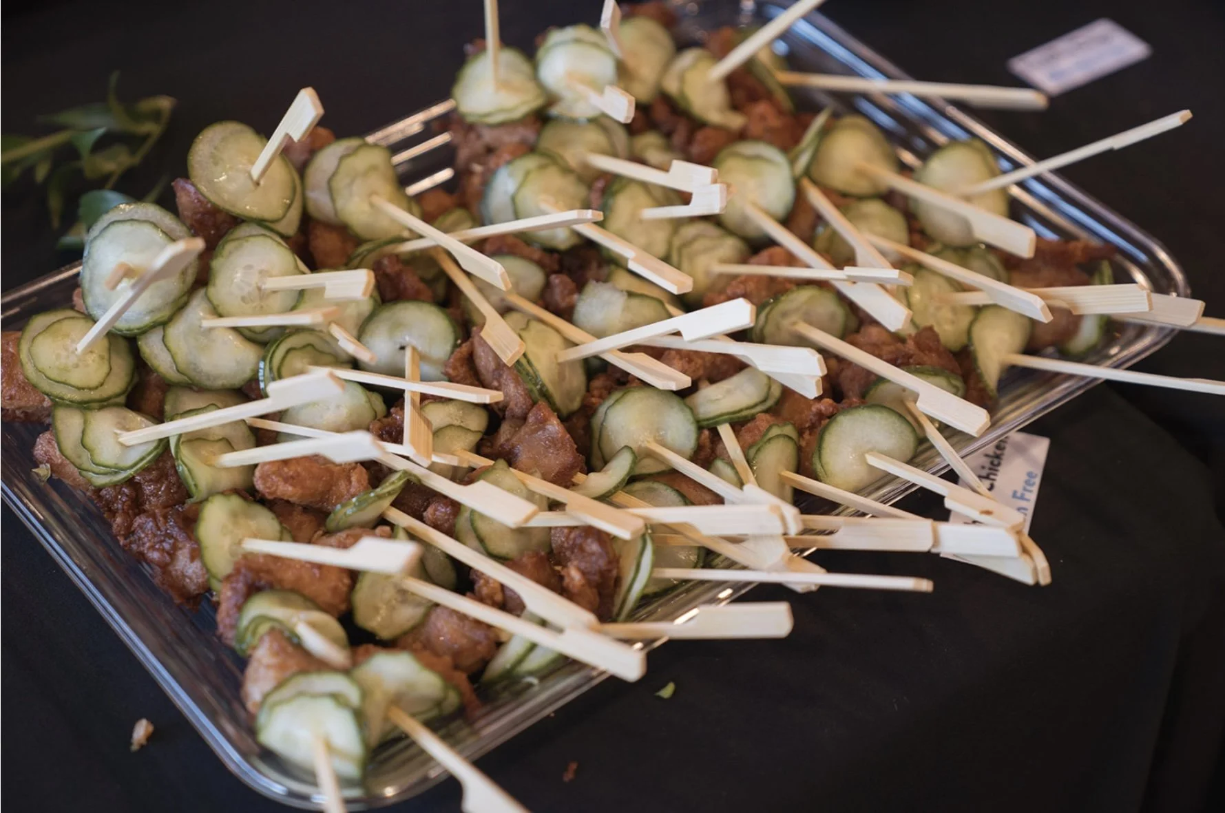 Skewers with pieces of fried chicken, cucumber slices, and green onions on a glass tray.