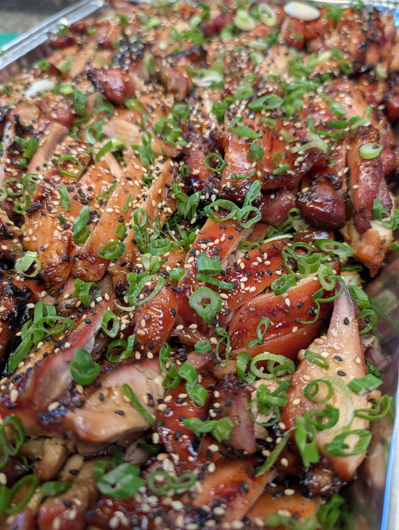 Close-up of grilled chicken pieces garnished with chopped green onions and sprinkled with sesame seeds and black pepper.