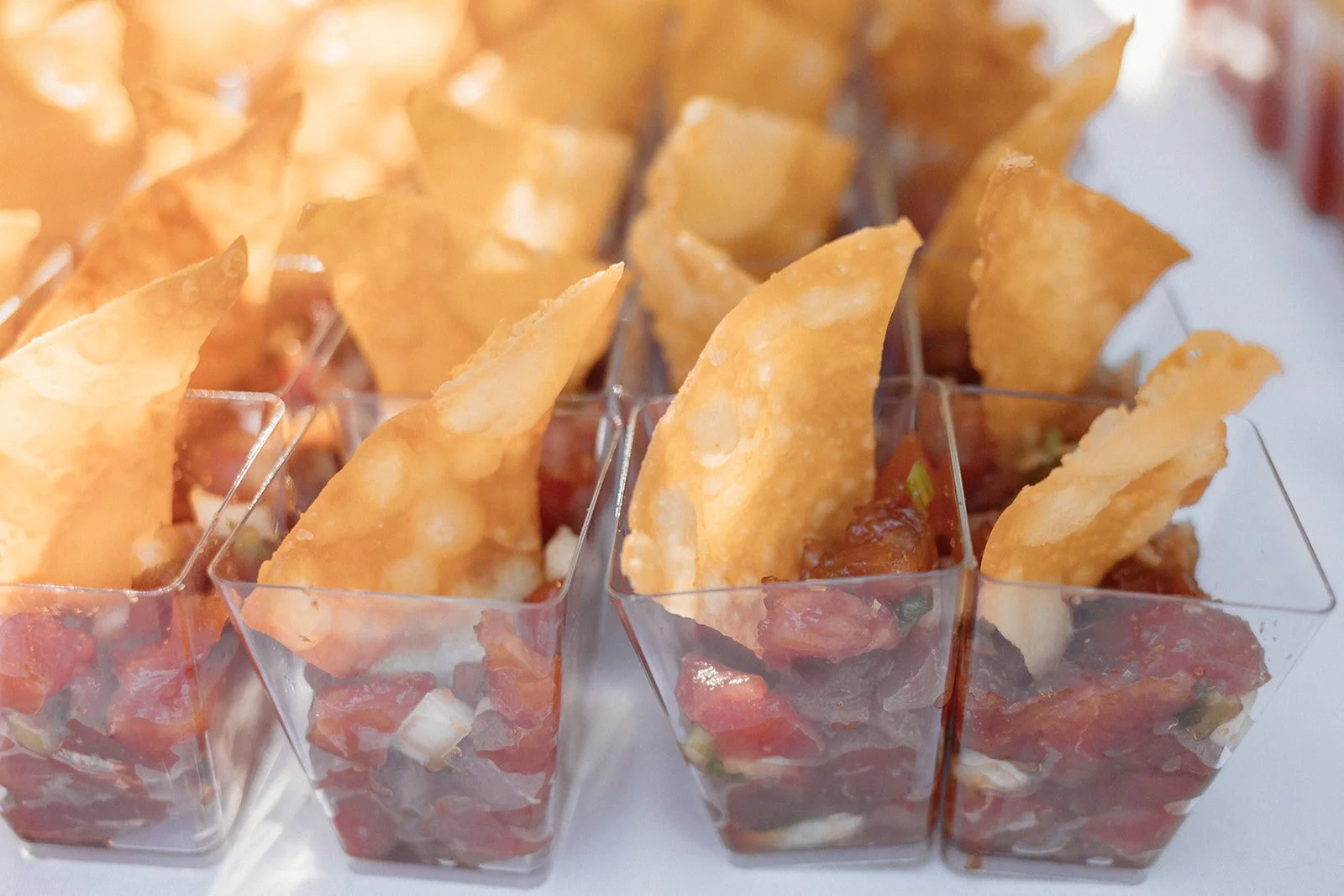 Individual servings of ceviche topped with crispy tortilla chips in clear plastic containers.