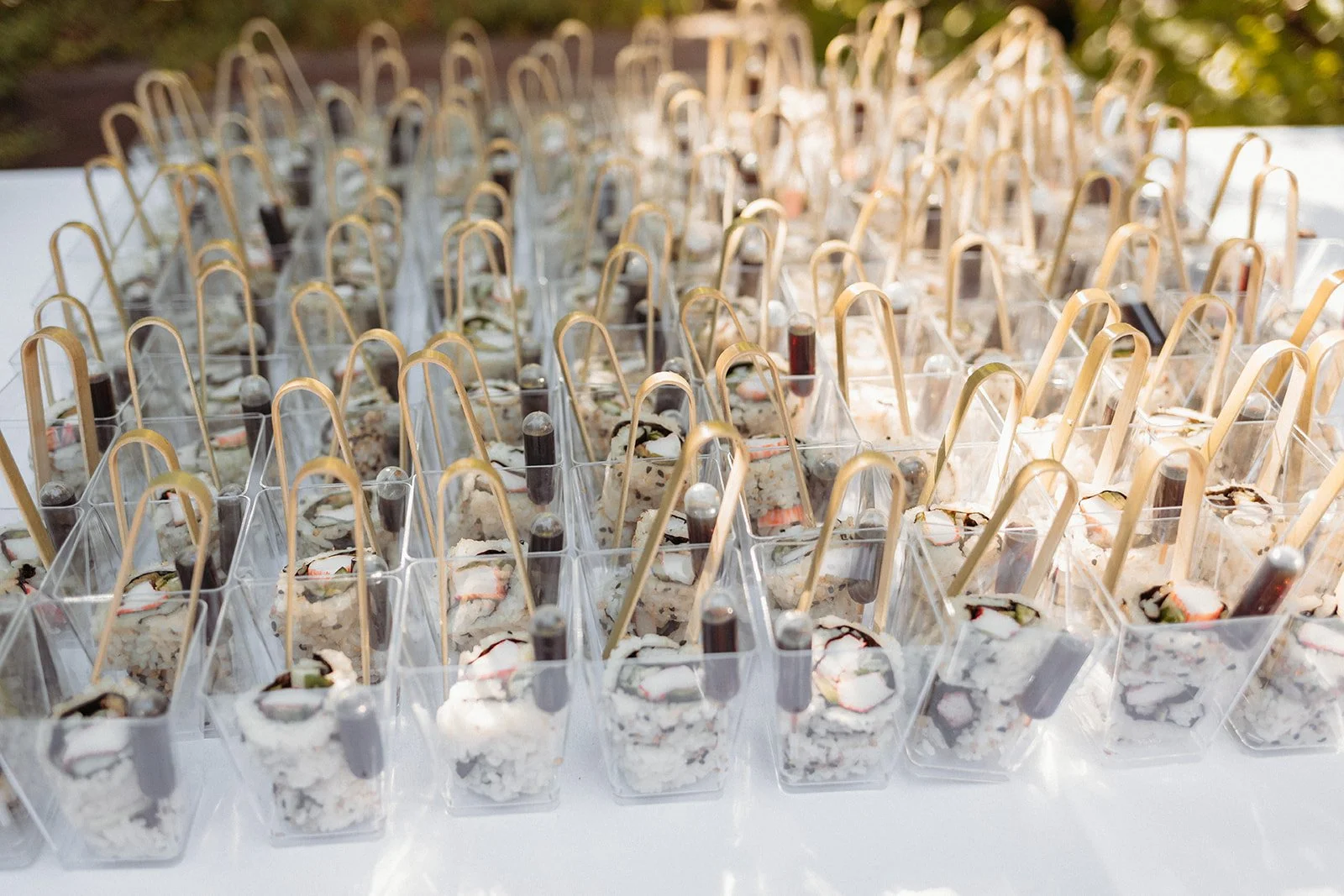 Mini sushi servings in small clear containers with gold-colored appetizer forks.