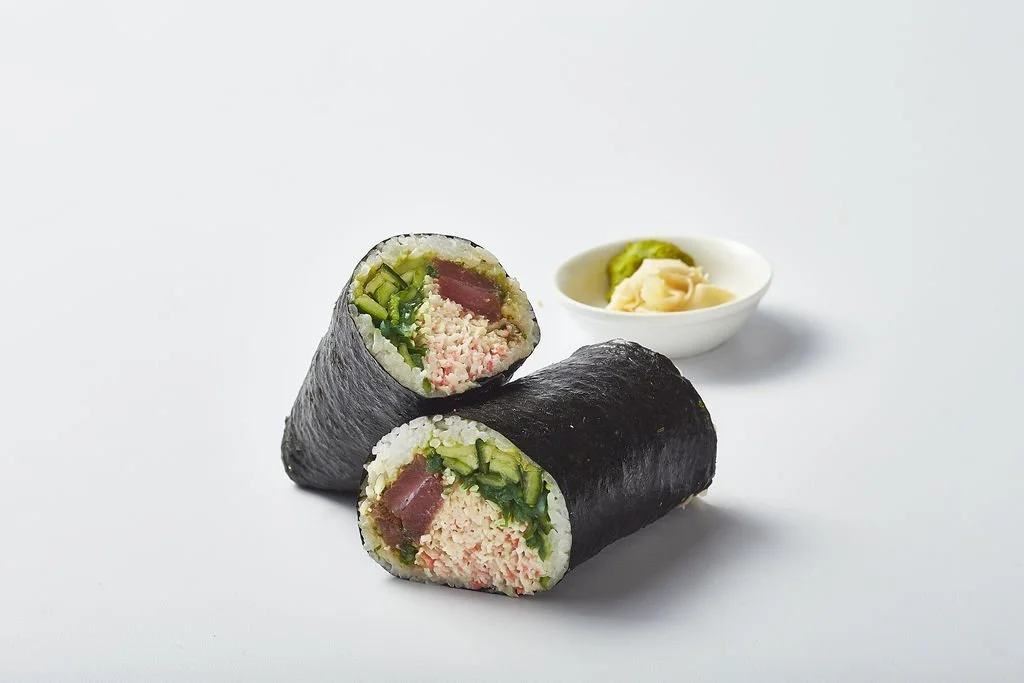 Sushi rolls with seaweed wrapping, filled with rice, cucumber, imitation crab, and raw fish, served with pickled ginger and wasabi in a small dish.