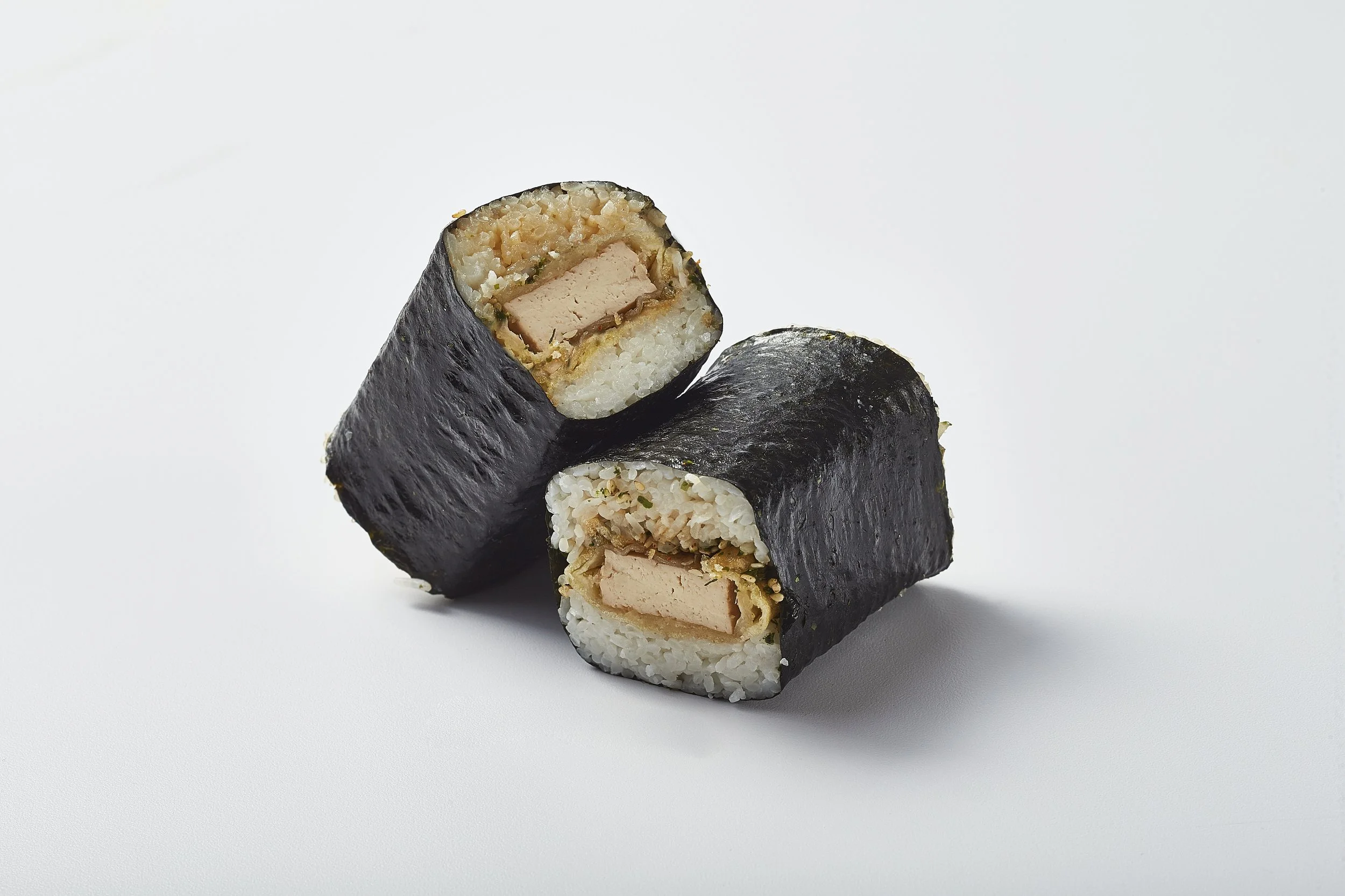 Two pieces of sushi roll with seaweed wrapping, rice, and filling including tofu, on a white background.