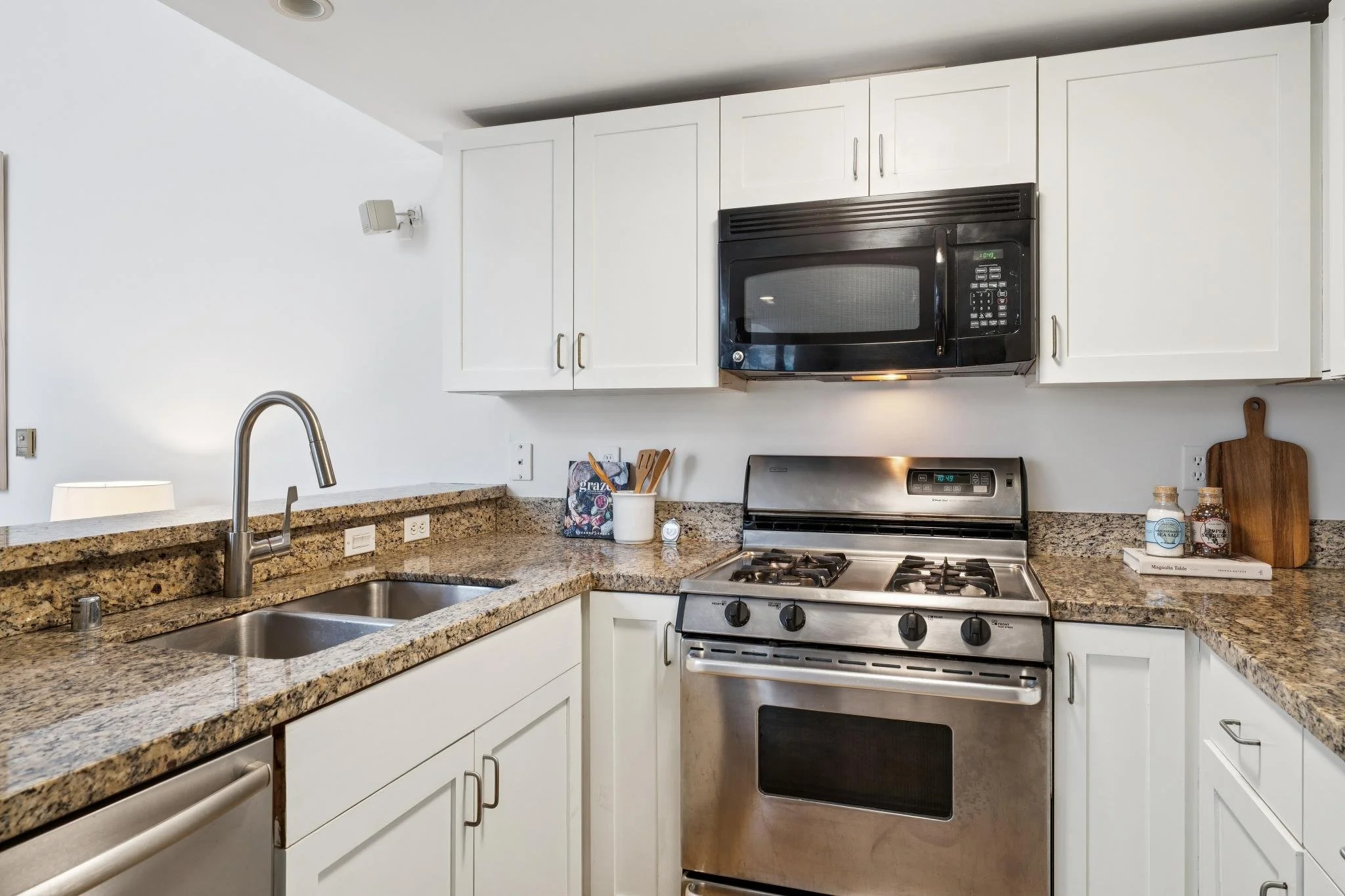 Kitchen with granite countertops, white cabinets, stainless steel gas stove, microwave, and double sink, kitchen accessories on the counter.