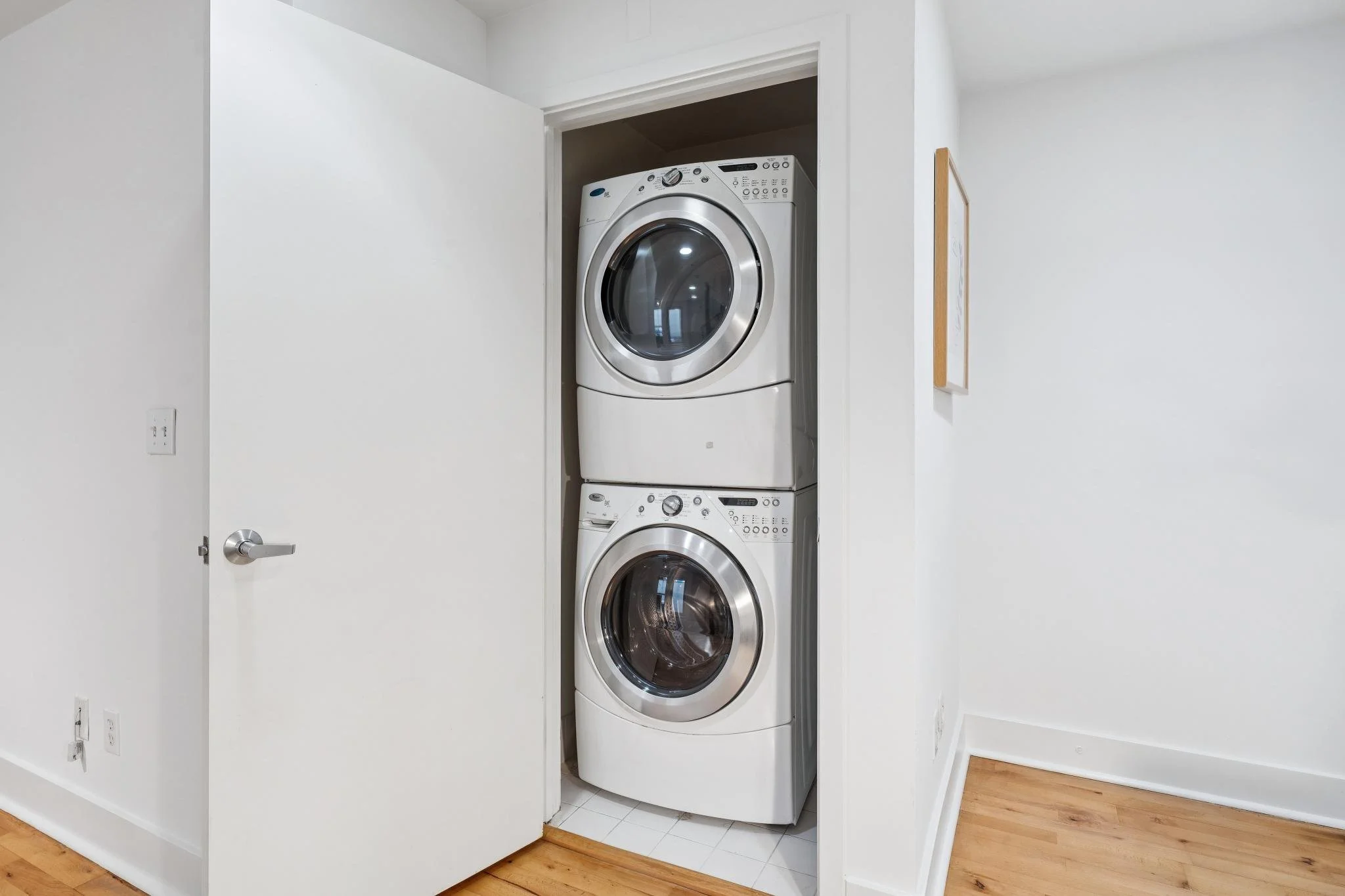 Stacked washer and dryer inside a laundry closet with a white door and white walls.
