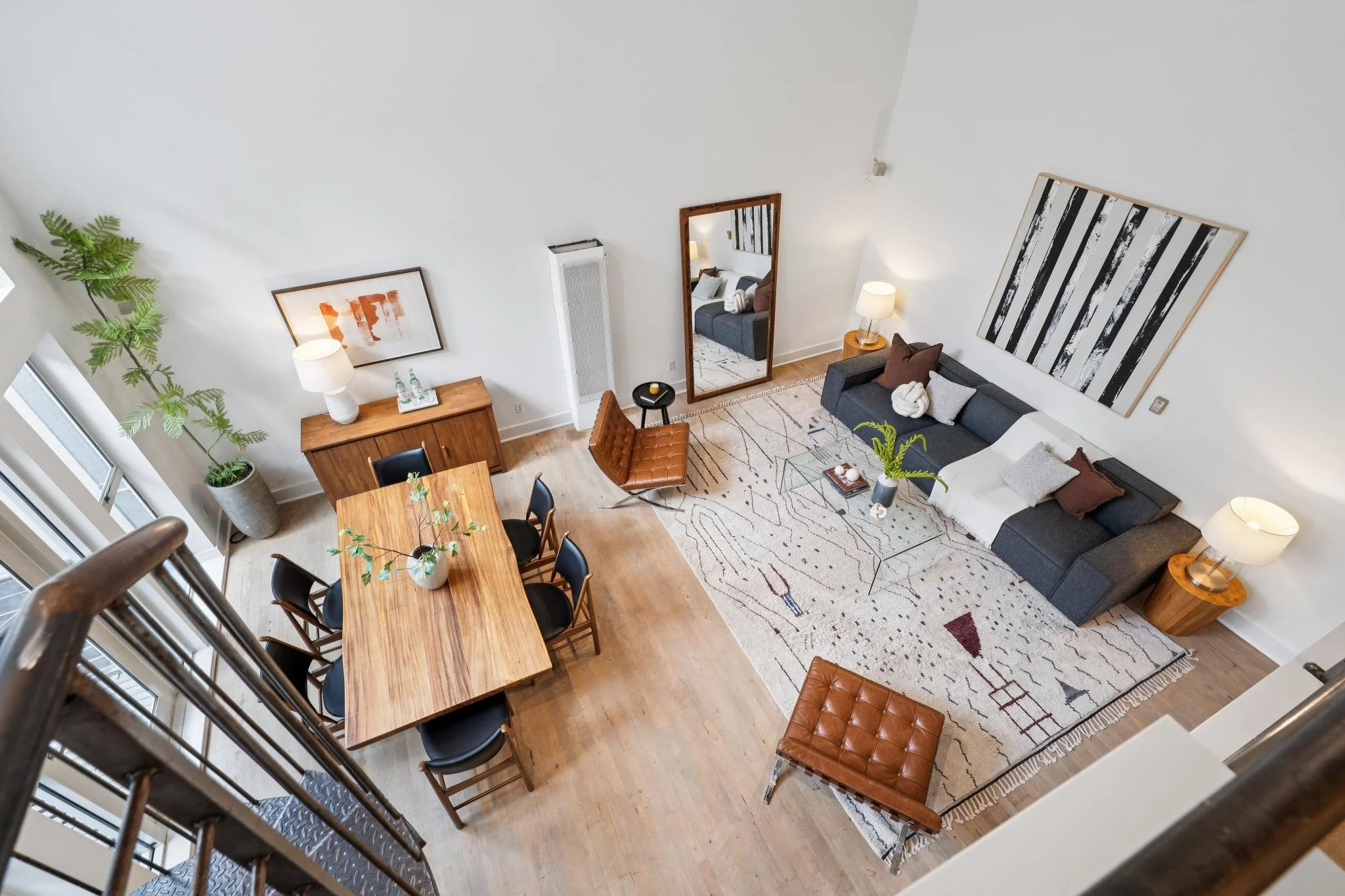 A spacious, modern living room with a dining area, gray sofa, wooden furniture, area rug, and artwork on white walls.