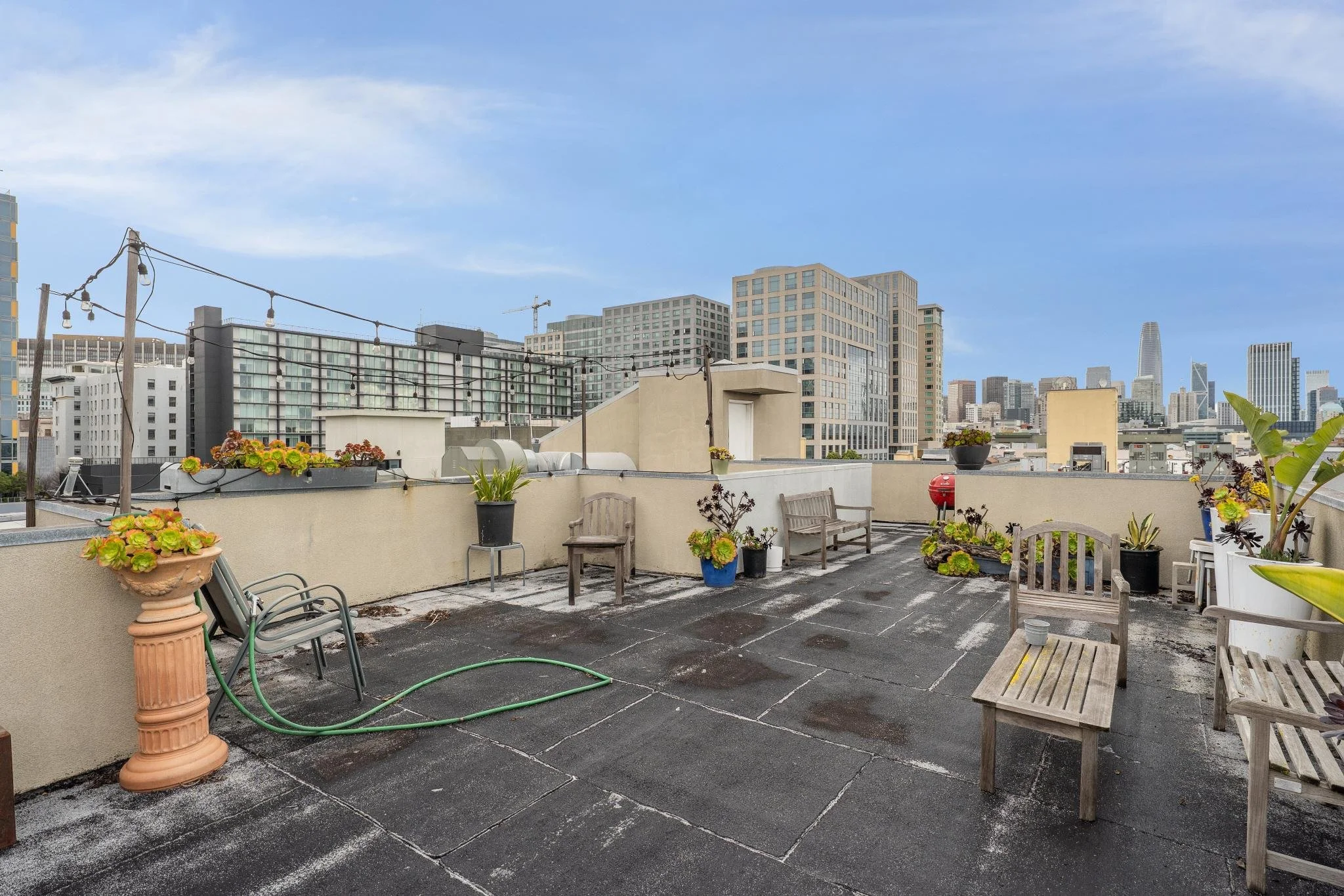 City rooftop with outdoor seating and potted plants under a blue sky.