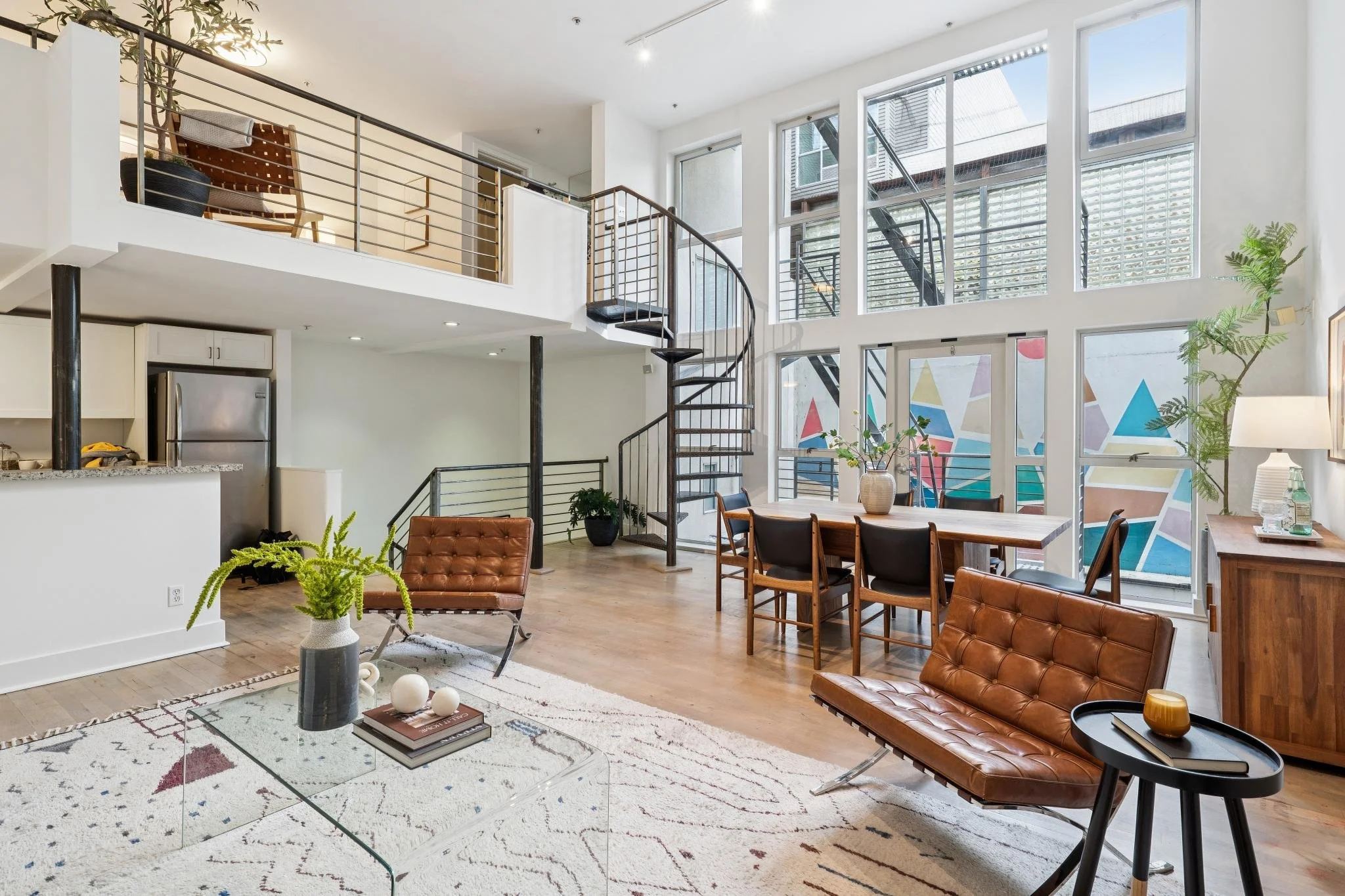 Open-concept living room with large windows, modern furniture, and a spiral staircase.