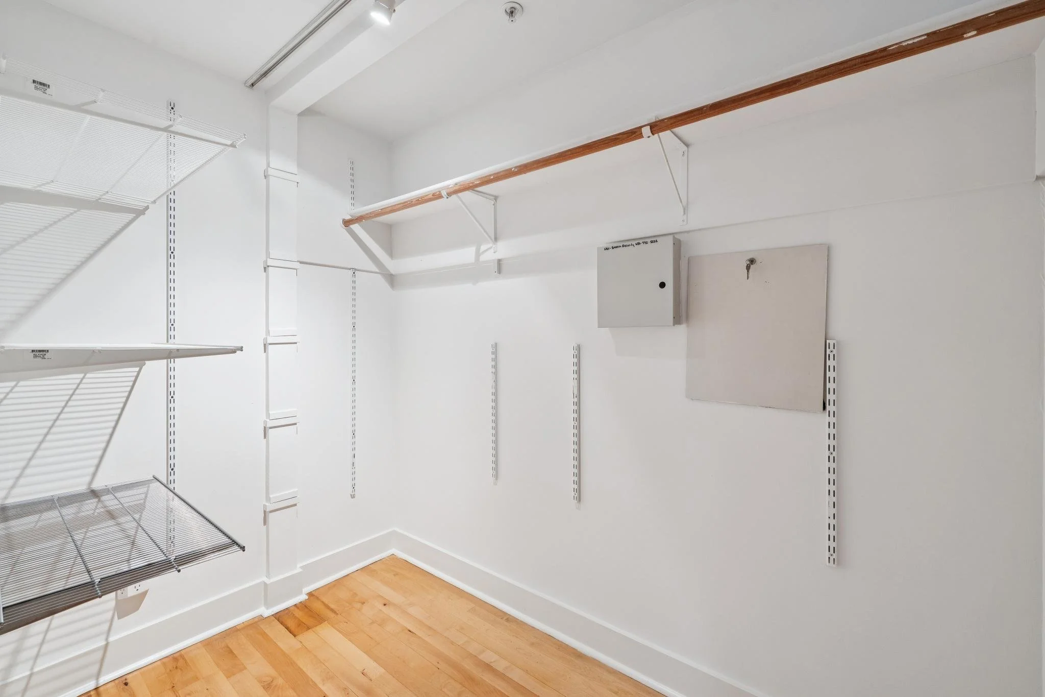 Empty walk-in closet with white walls, wire shelves, and wood flooring.