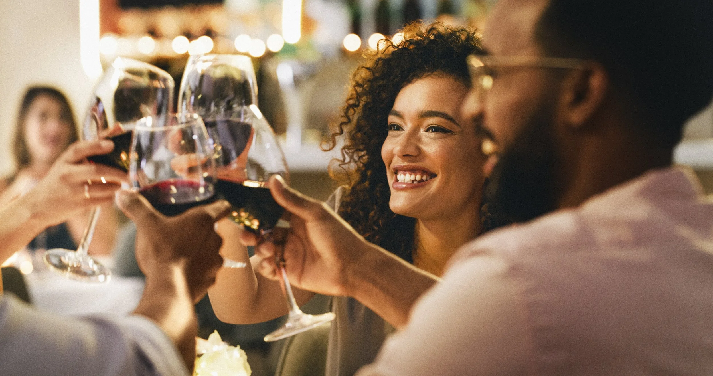 A group of friends celebrating and clinking glasses of red wine at a social gathering or dinner party, smiling and enjoying each other's company.