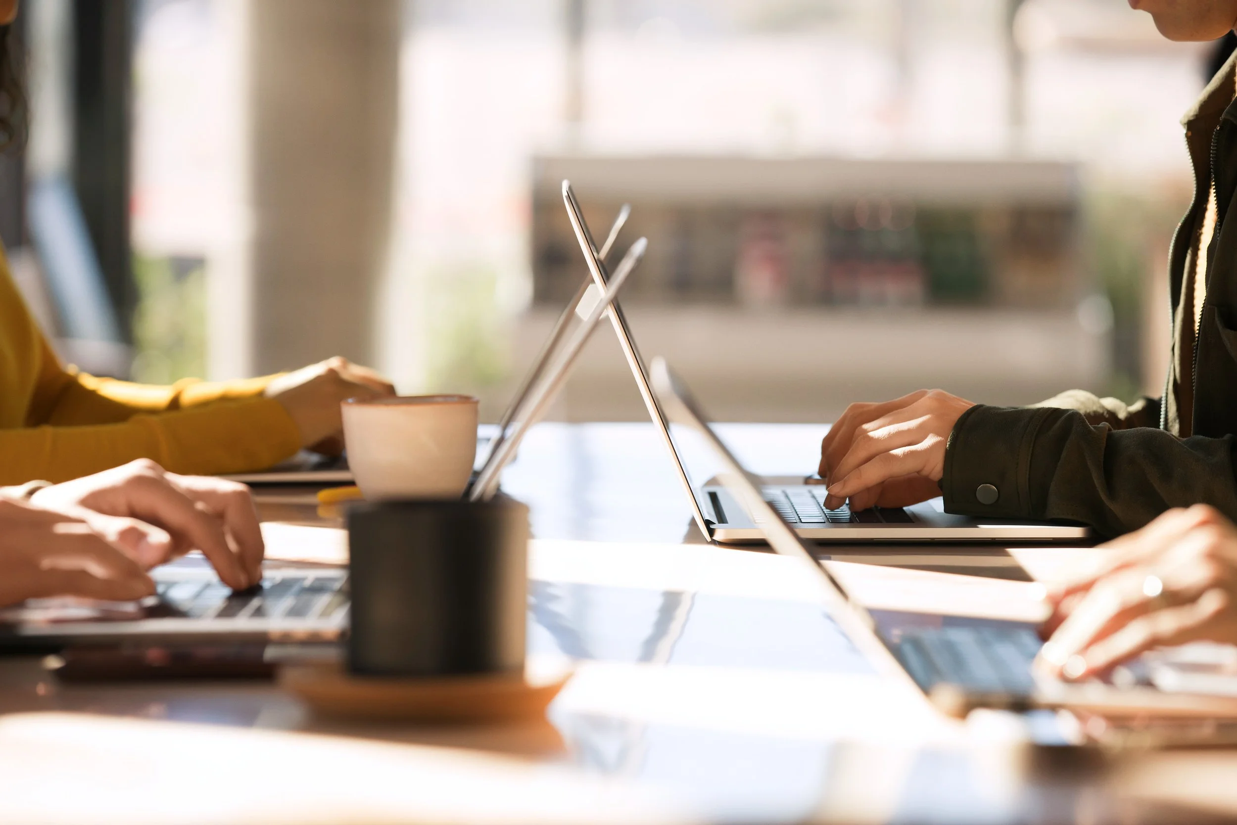 People working on laptops at a table in a well-lit space, possibly a cafe or meeting room.