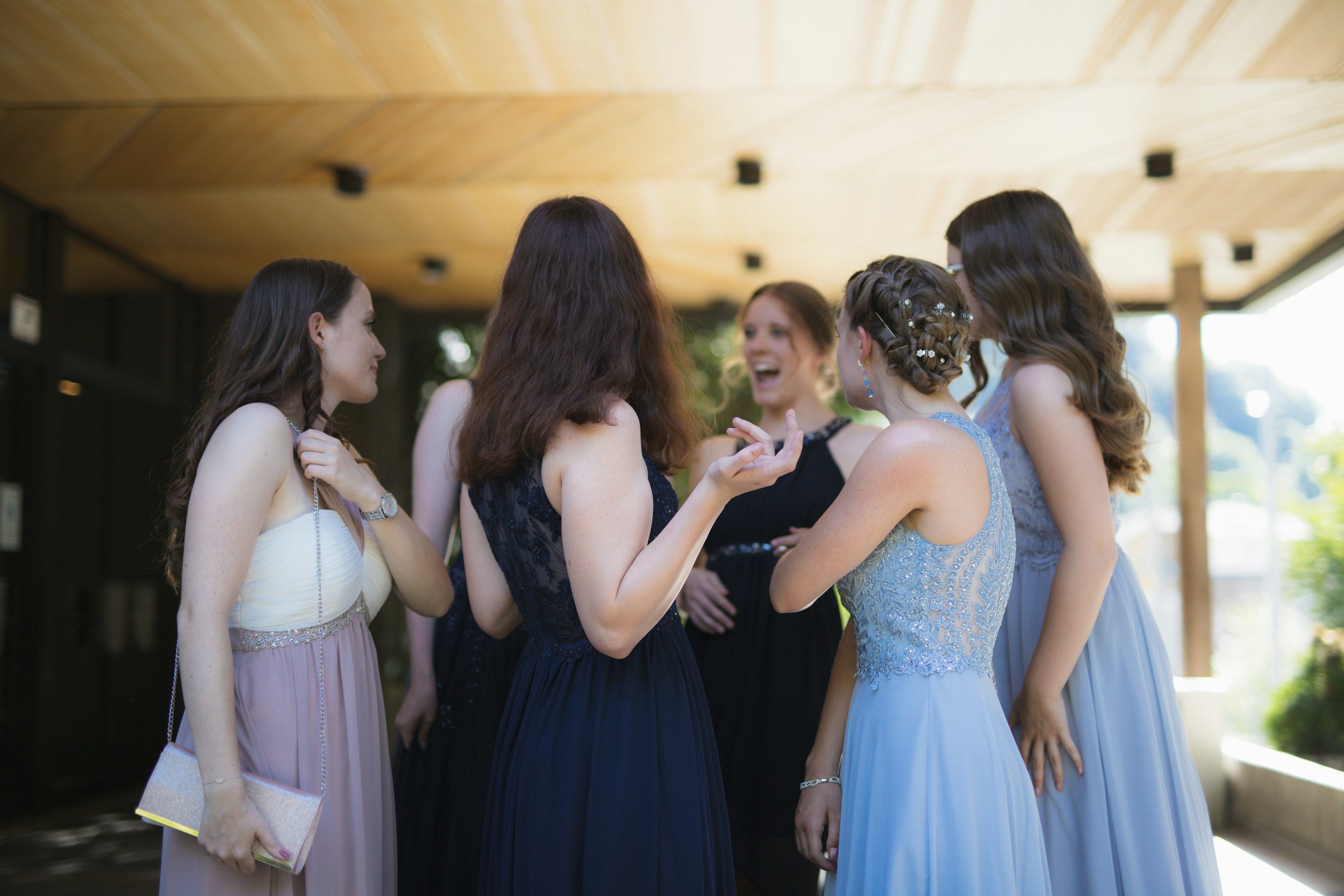 A group of women in evening dresses socializing outdoors under a wooden roof.