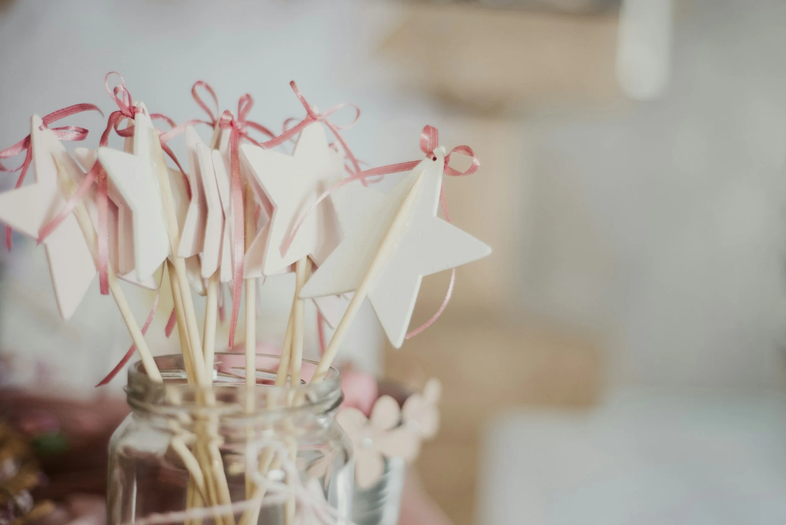 Close-up of white star-shaped cookies with pink ribbons on toothpick sticks in a glass jar.