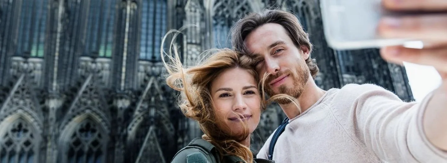 A young couple taking a selfie in front of a large Gothic cathedral.