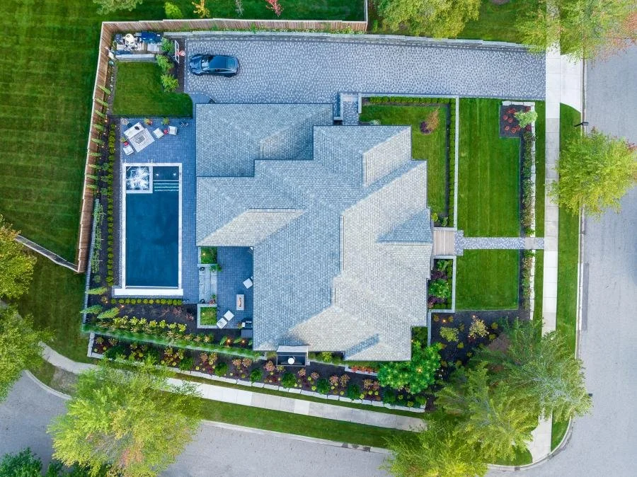 Aerial view of a house with a swimming pool, driveway, garden, and lush green lawn.