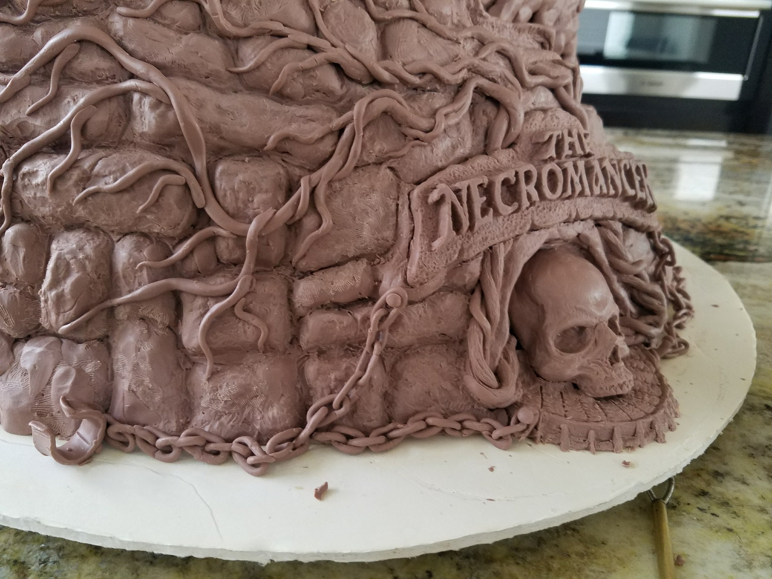 Close-up of a cake decorated with chocolate icing and intricate chocolate chains, with embossed letters that are partially visible.