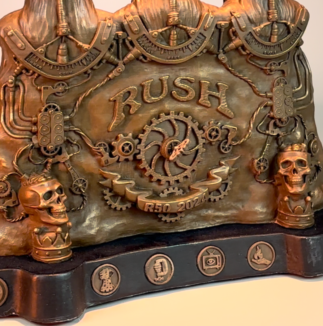 A decorative metallic plaque with gears, skulls, and mechanical details, featuring the word 'RUSH' and the inscription 'R50 2024'.