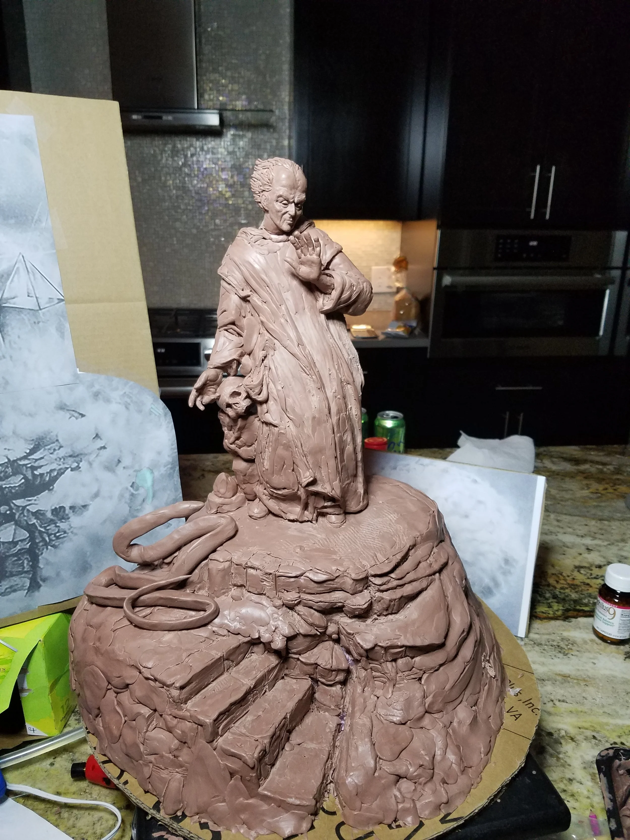 Clay sculpture of a person with spiky hair making a gesture with a raised hand, placed on a work surface in a kitchen setting.