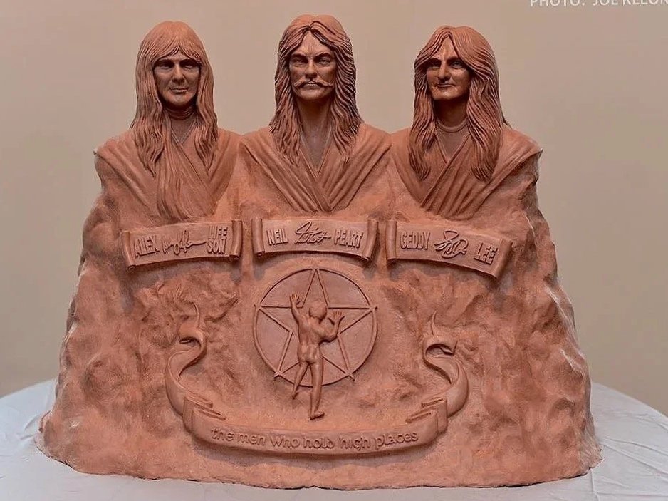 Terracotta sculpture of the members of Led Zeppelin, featuring Robert Plant, Jimmy Page, and John Paul Jones, with a central figure of a man with arms raised, and the quote 'The men who hold high places' below.