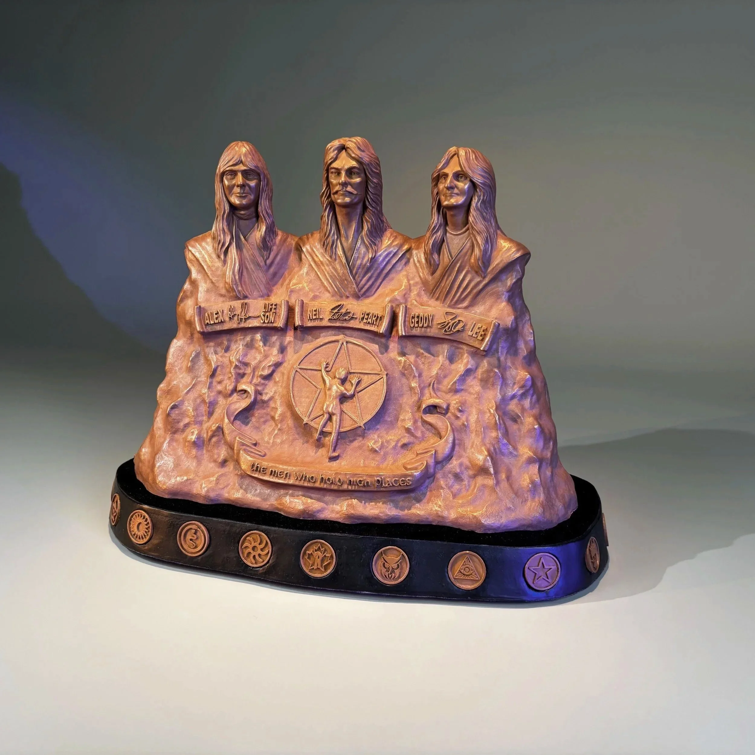 Bronze memorial sculpture of three men with long hair, featured on a black circular base with various planetary and star symbols, and engraved names and phrases.