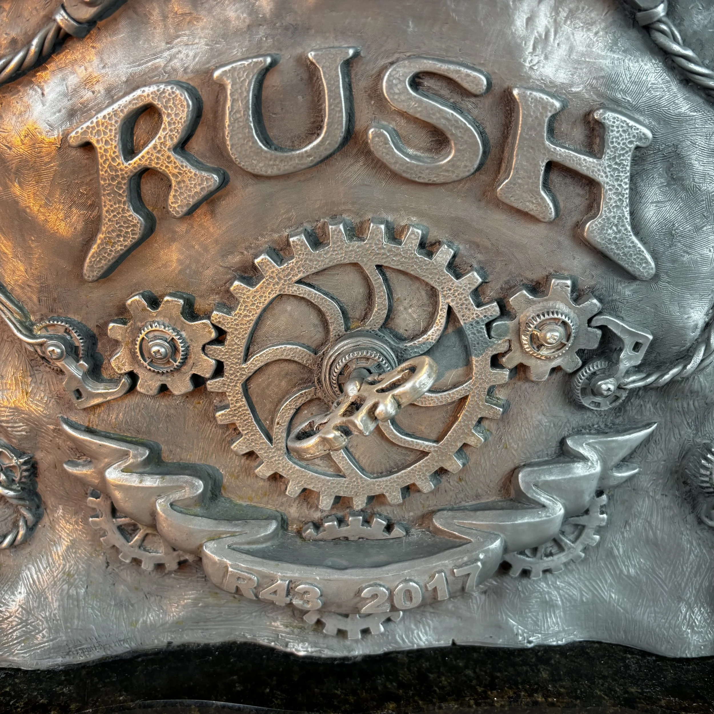 Close-up of metallic gears on a silver surface with the words 'RUSH' and other text visible on one gear.