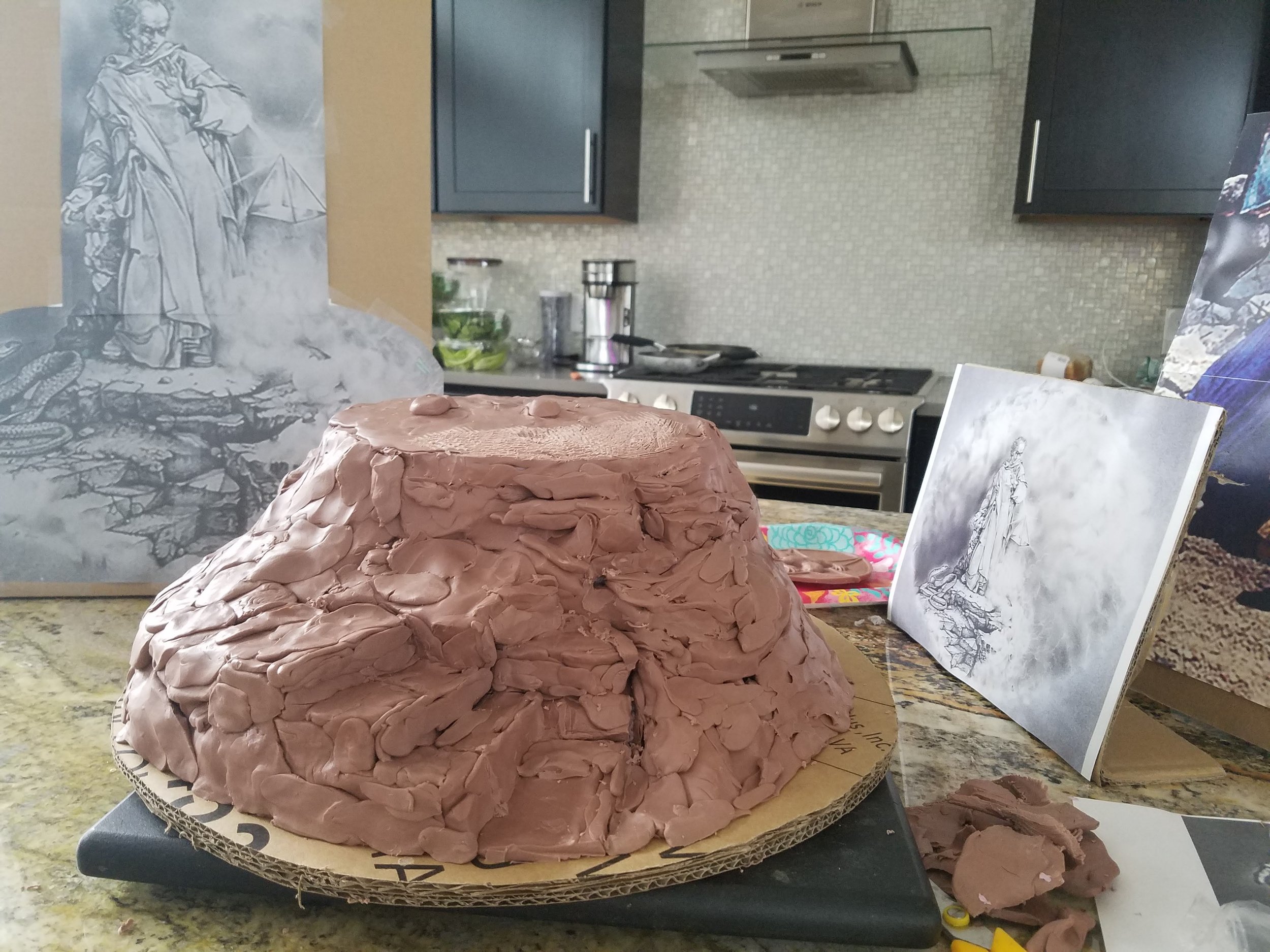 Unfinished sculpture of a woman in a long dress, sitting with her hand on her lap, drawn with pencil on paper, displayed against a kitchen backsplash with a stove and countertop in the background.