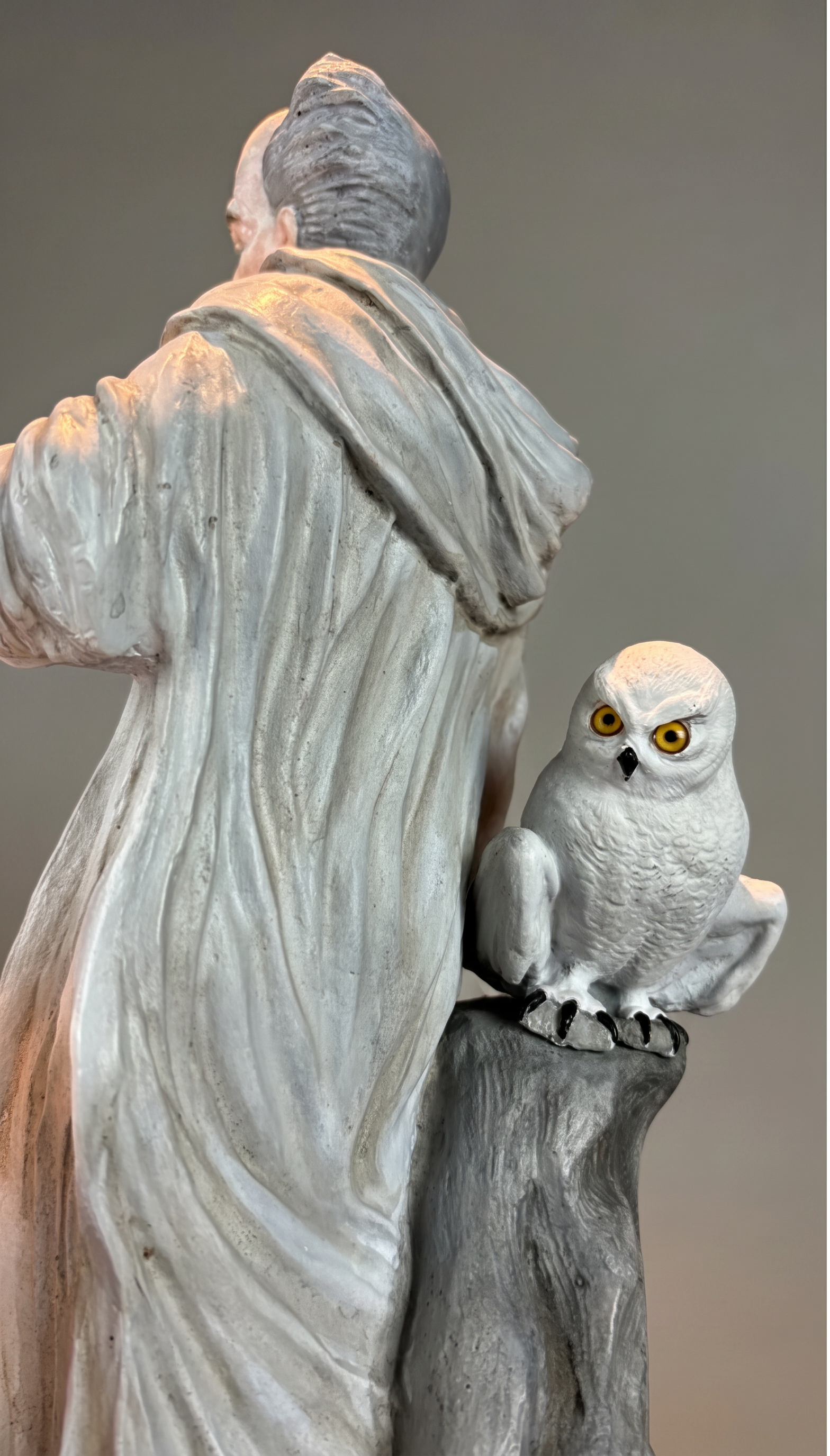 A sculpture of an elderly man with gray hair, wearing a long garment, holding a white owl with yellow eyes on his arm.