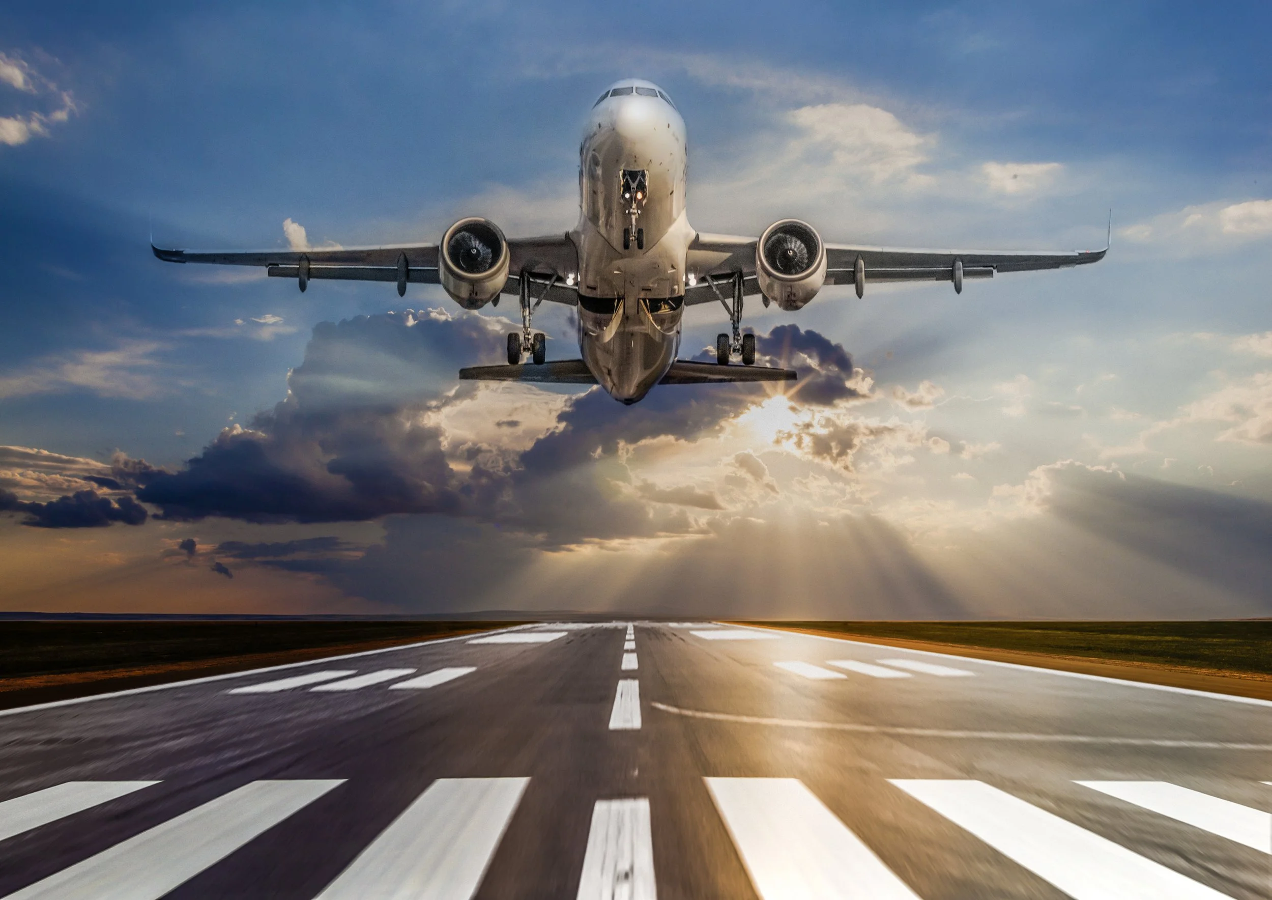 A commercial airplane taking off from a runway during sunset, with clouds in the sky.