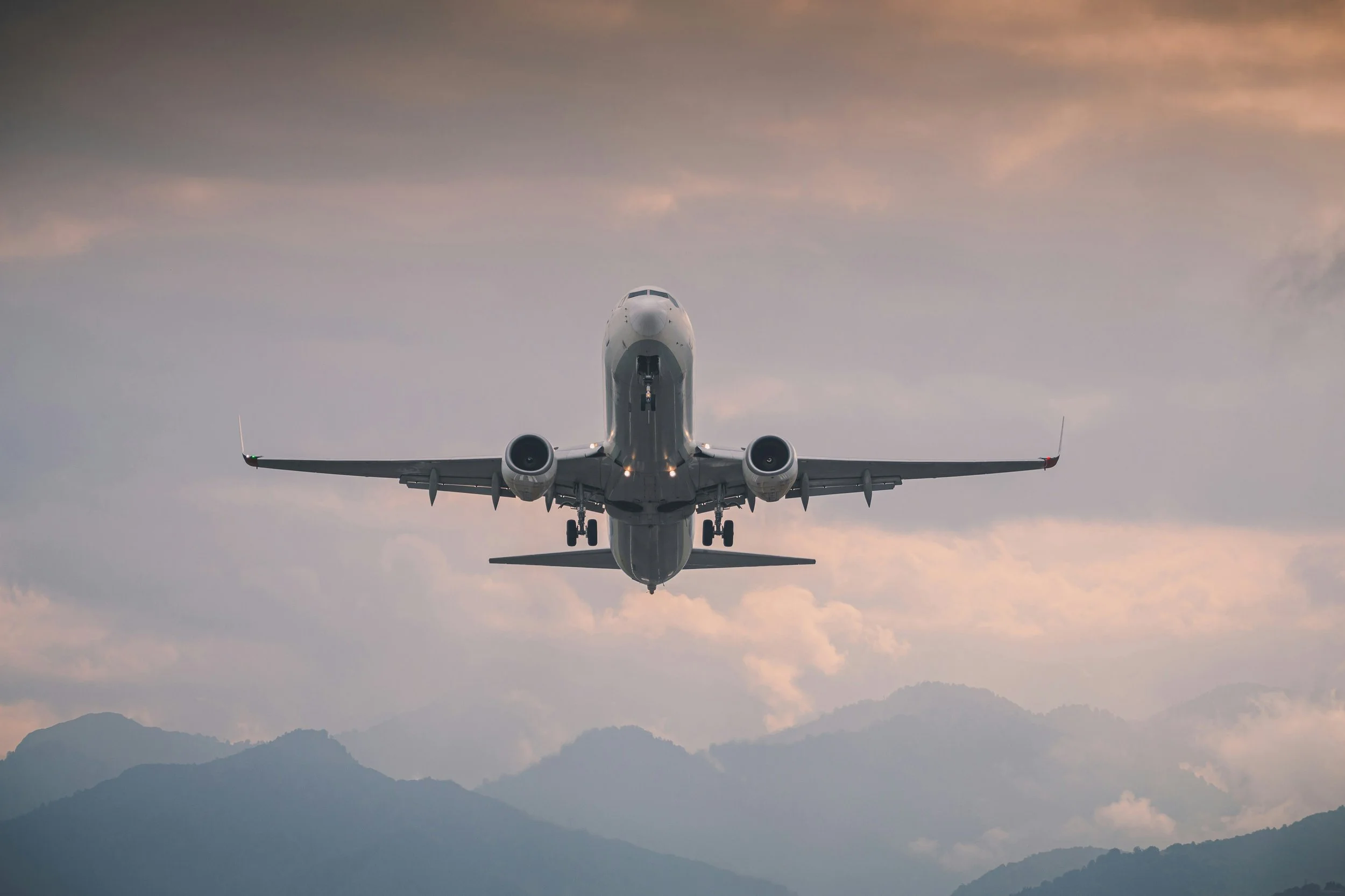 An airplane flying low over mountains during sunset or sunrise.
