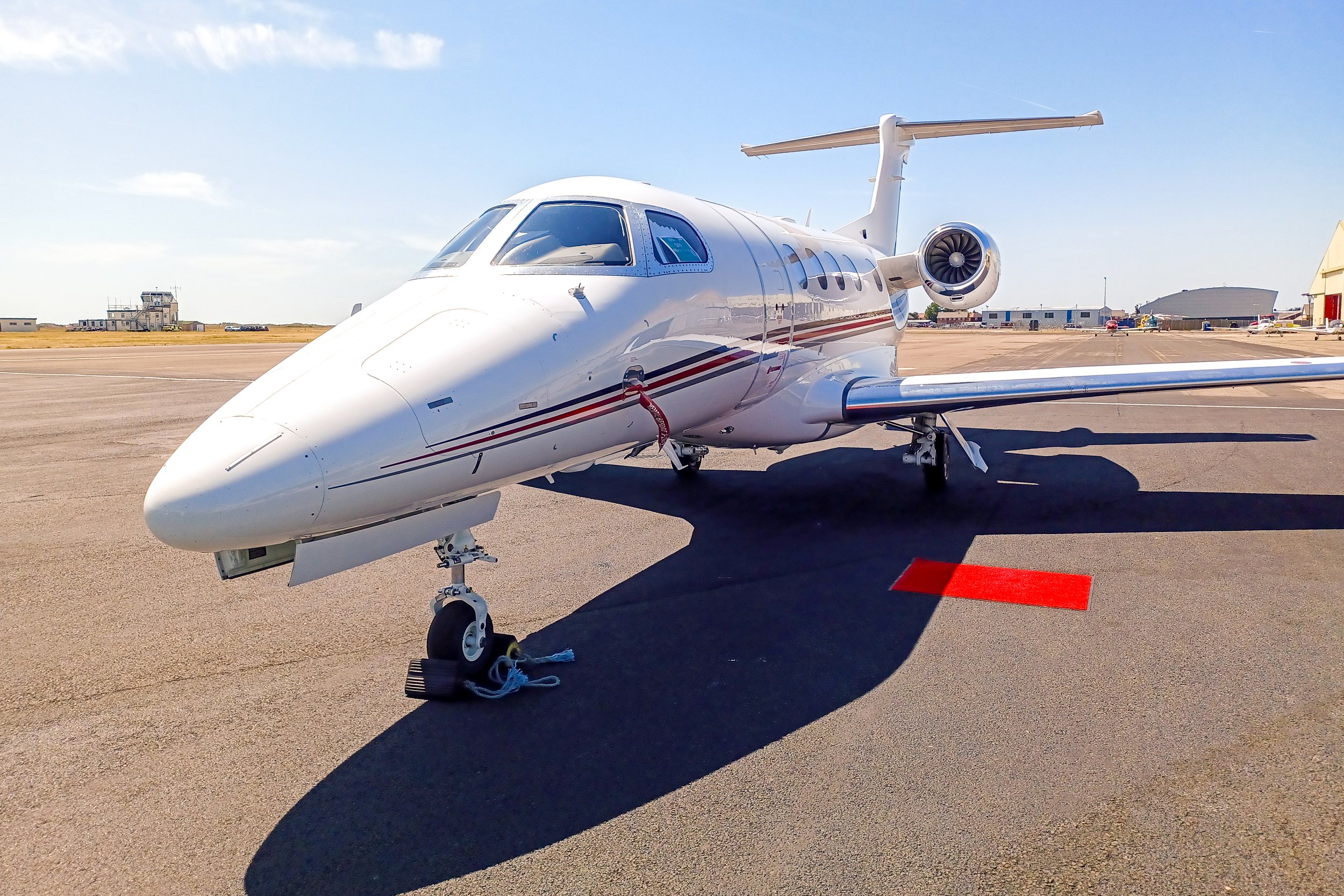 A white private jet airplane parked on an airport tarmac under a blue sky with few clouds.