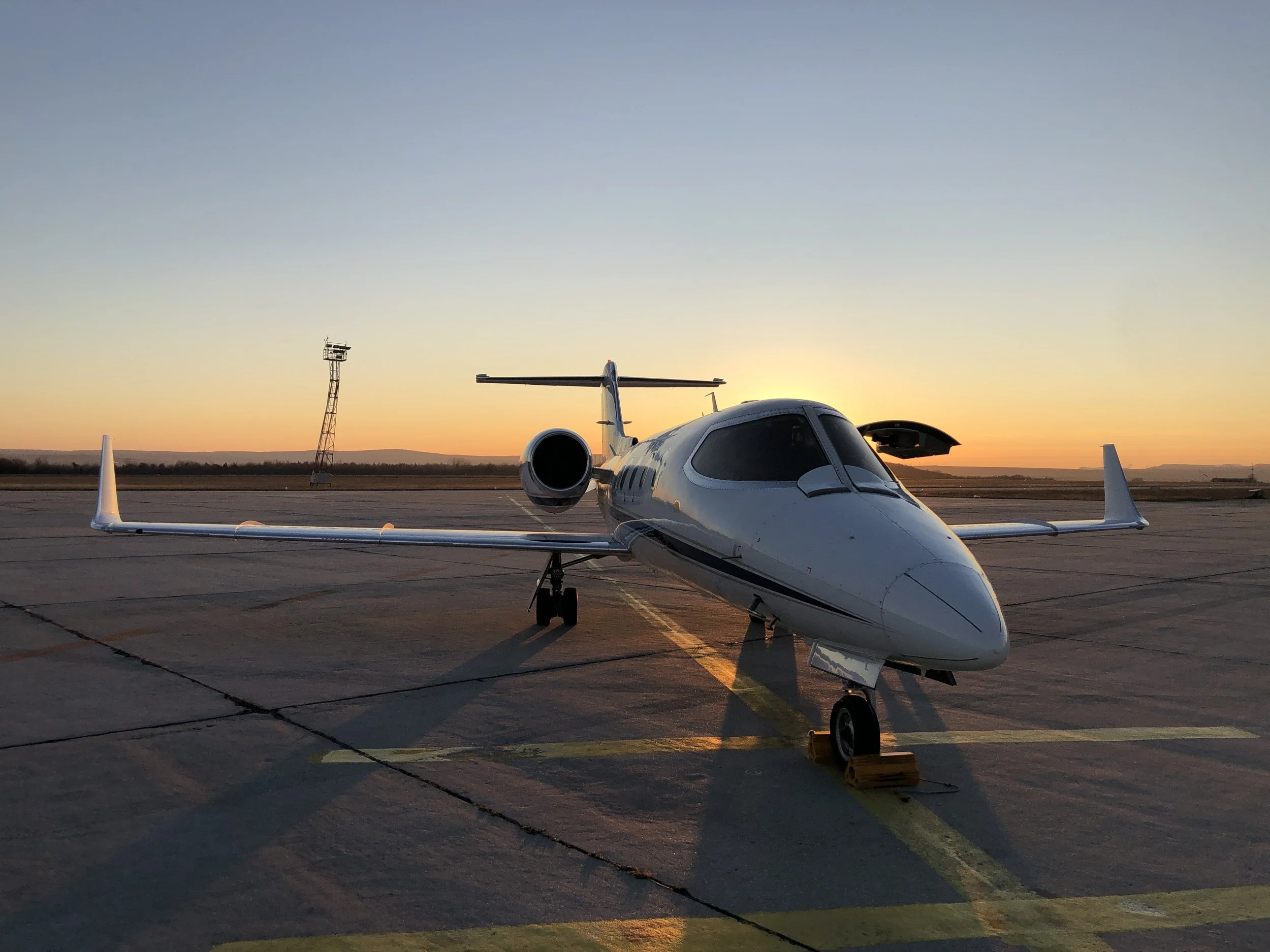Private jet parked on the tarmac at sunset with a radar tower in the background.