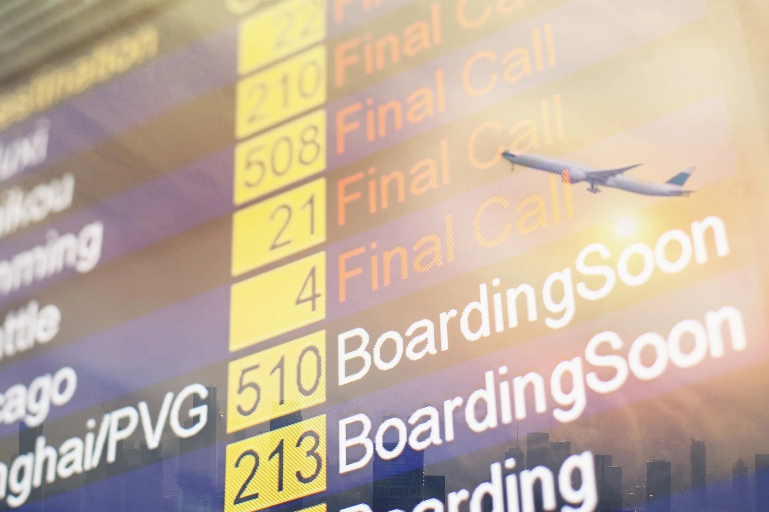 A flight information display board showing flight numbers, destinations, and statuses with an airplane flying in the background at sunset.