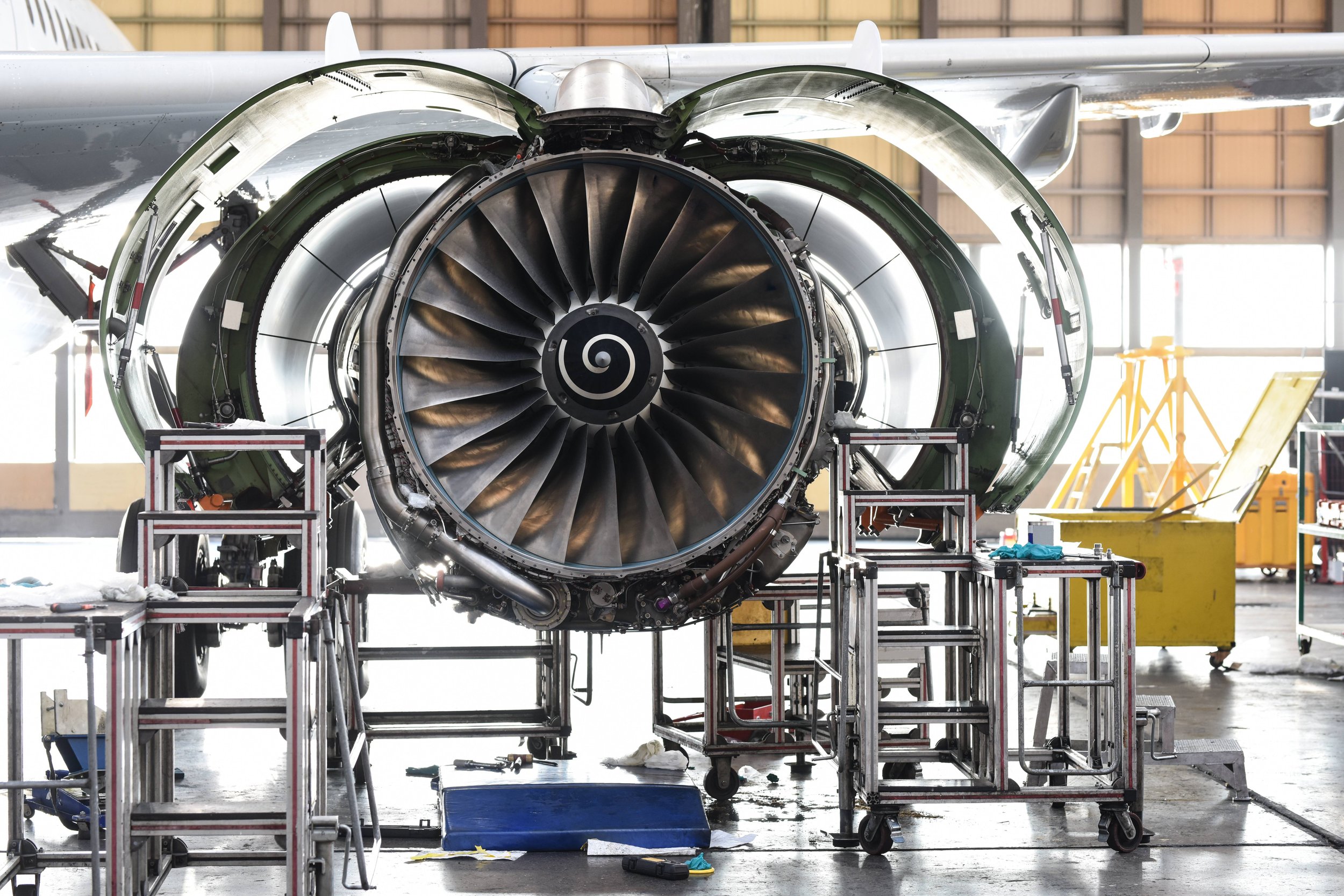 Close-up of a jet engine in an aircraft assembly hangar, surrounded by scaffolding and equipment.