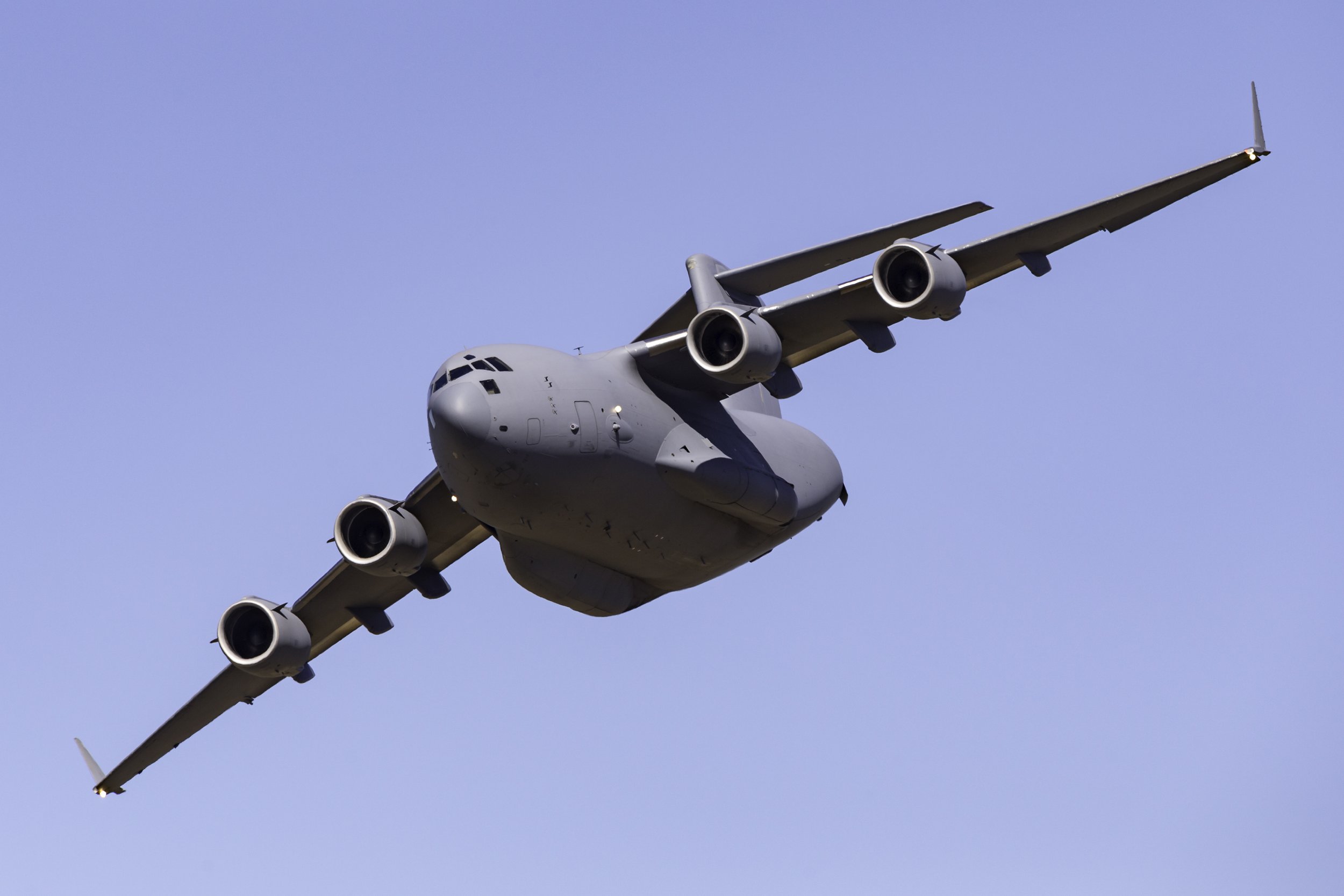 A large gray military cargo airplane flying in a clear blue sky.