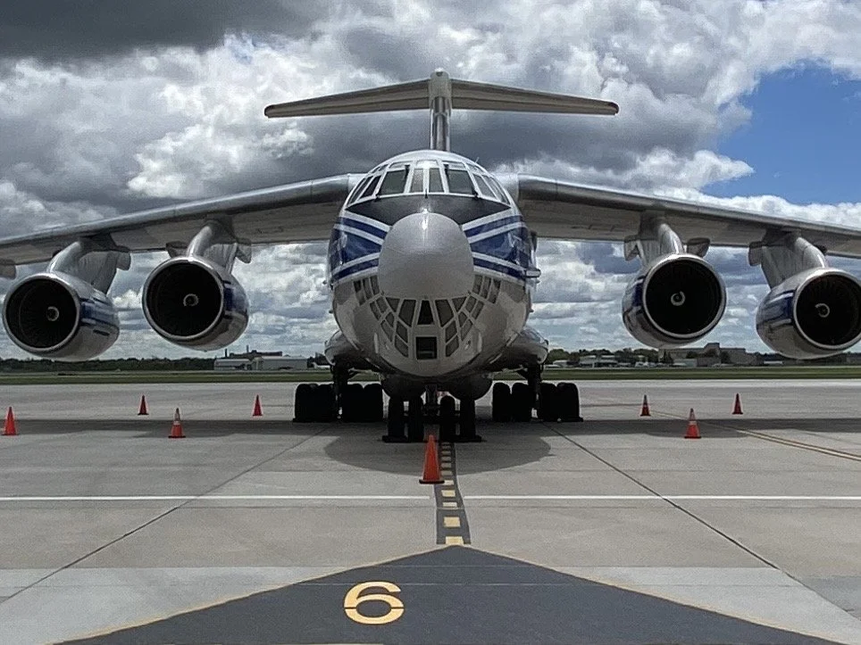 Front view of a large cargo airplane parked on the tarmac with orange cones around it, under a cloudy sky.
