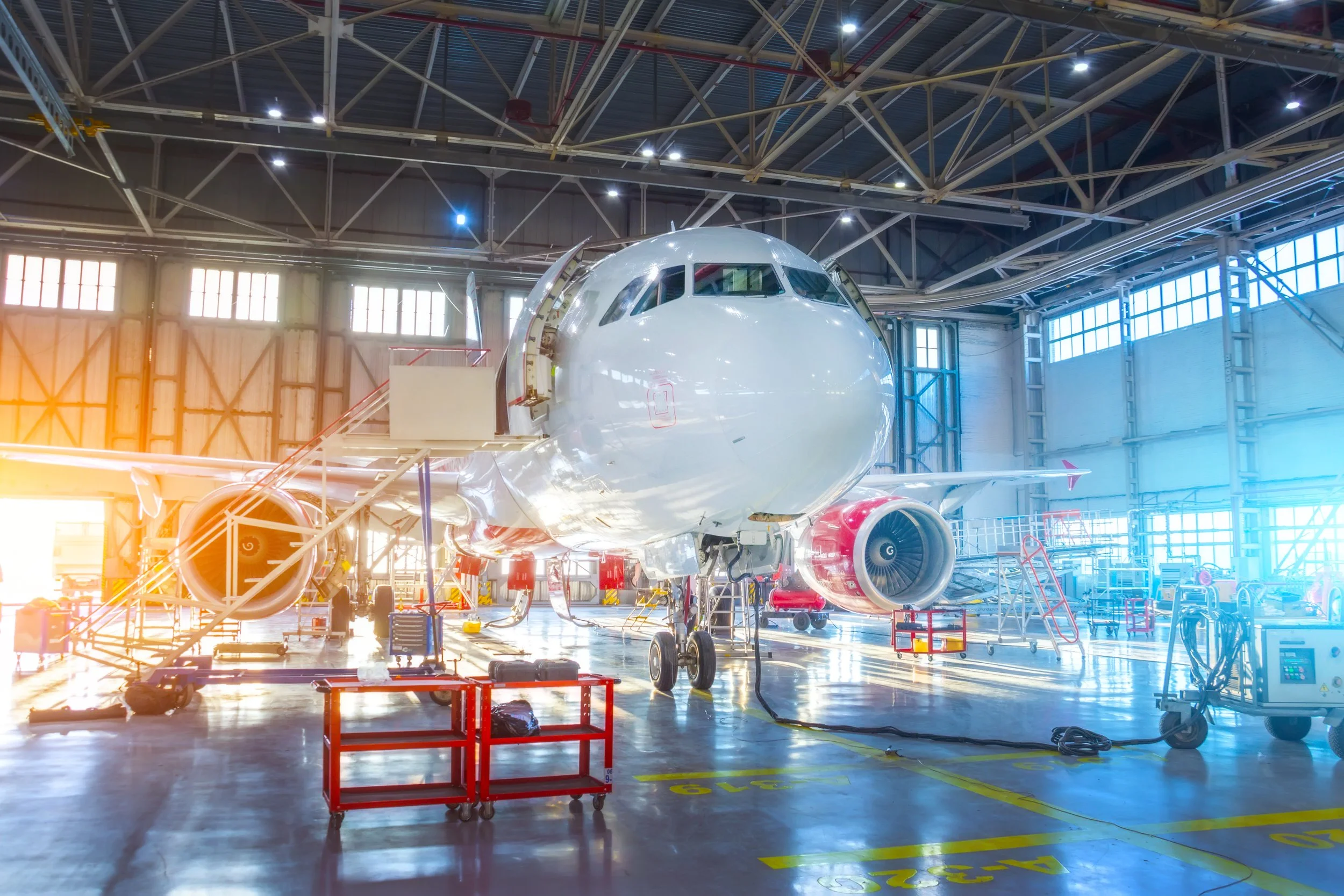 An airplane inside a large hangar, surrounded by various maintenance equipment and tools.