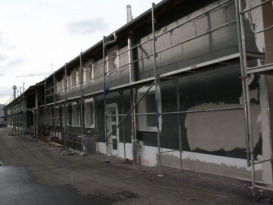 Baugerüst vor einem Gebäude, das renoviert wird, mit dunkler Fassade und mehreren Fenstern.