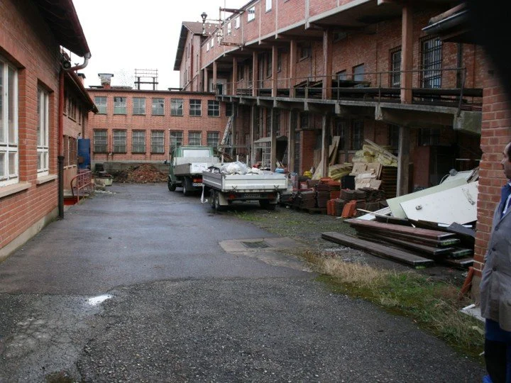 Baustelle im Innenhof eines roten Backsteingebäudes mit Baugerüsten, Baumaterialien und Fahrzeugen.
