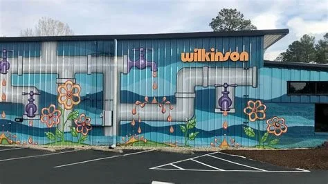 Colorful mural on the side of a building depicting flowers, pipes, and water-themed elements with the name 'Wilkinson' in orange letters.