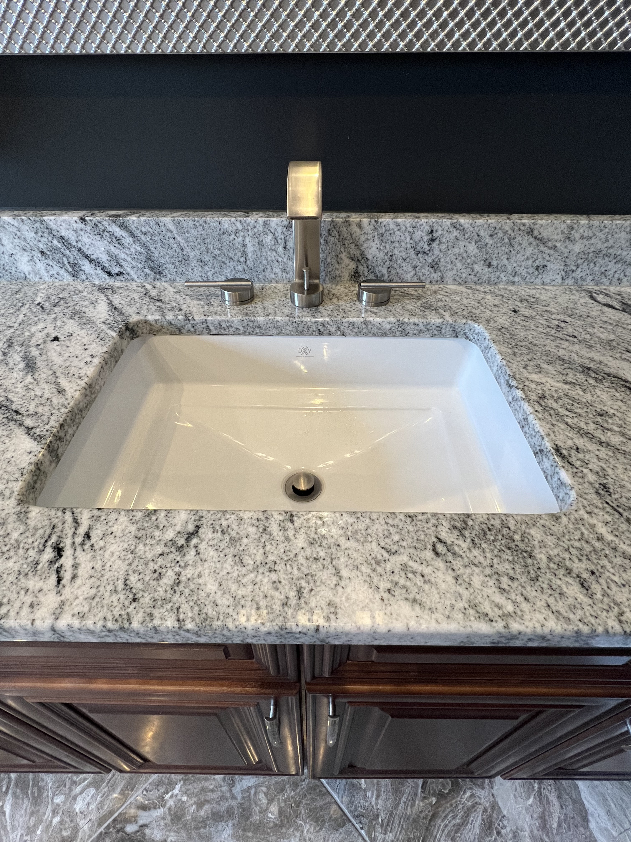 A kitchen countertop with a white undermount sink, a modern brushed nickel faucet, and dark wooden cabinets below.